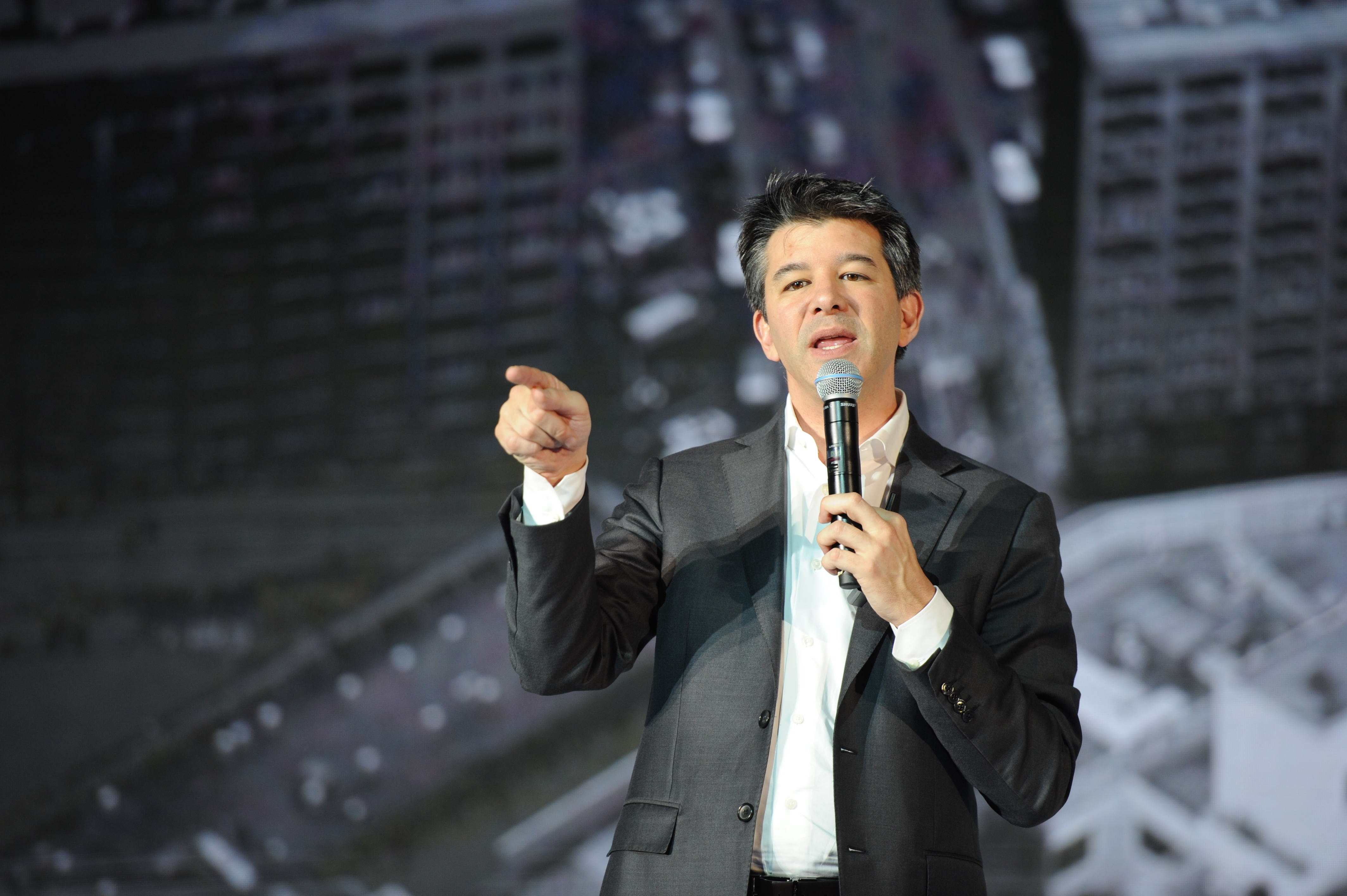 Former Uber CEO Travis Kalanick onstage holding a microphone and pointing at the audience
