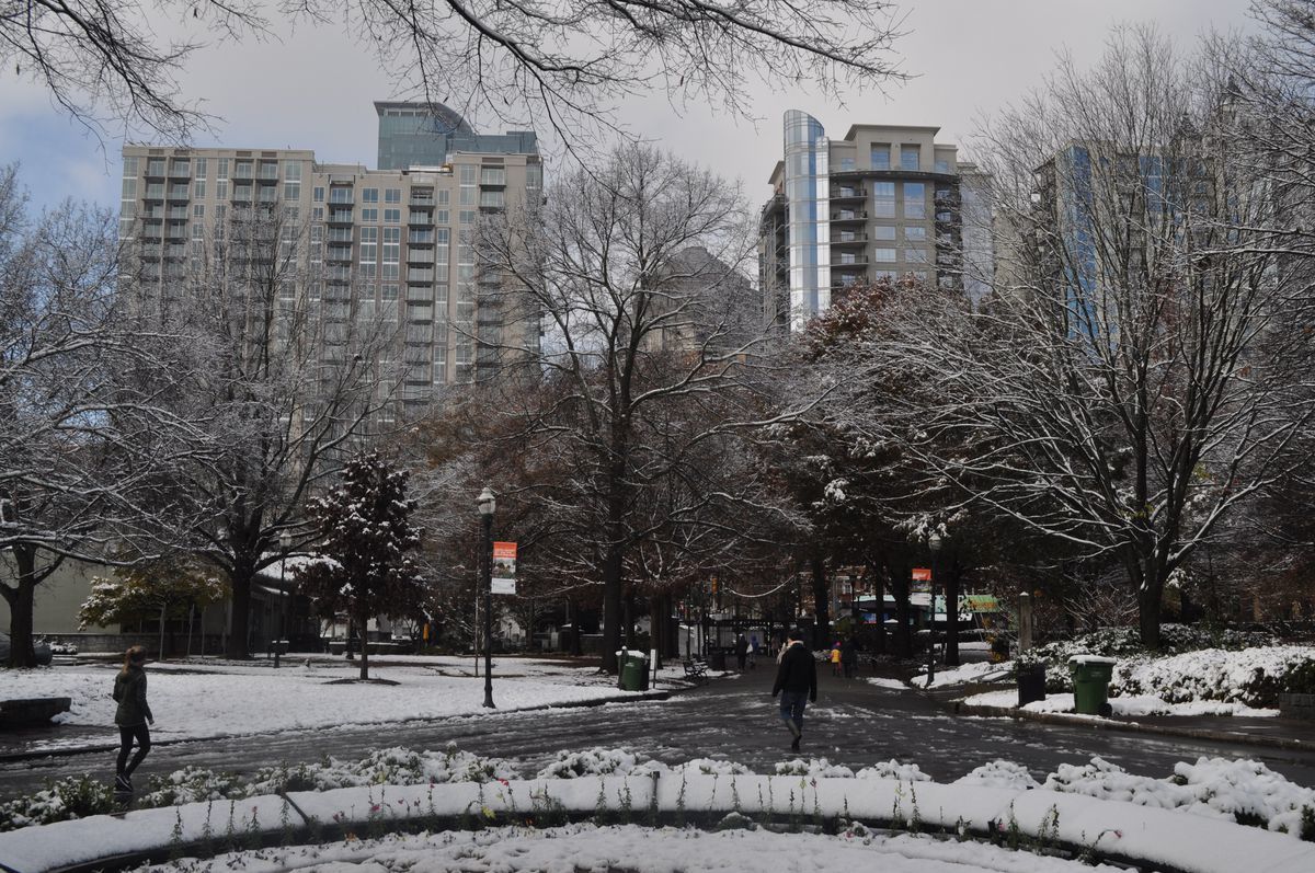 A park and tall glassy building covered in snow, with trees and joggers in the foreground. 