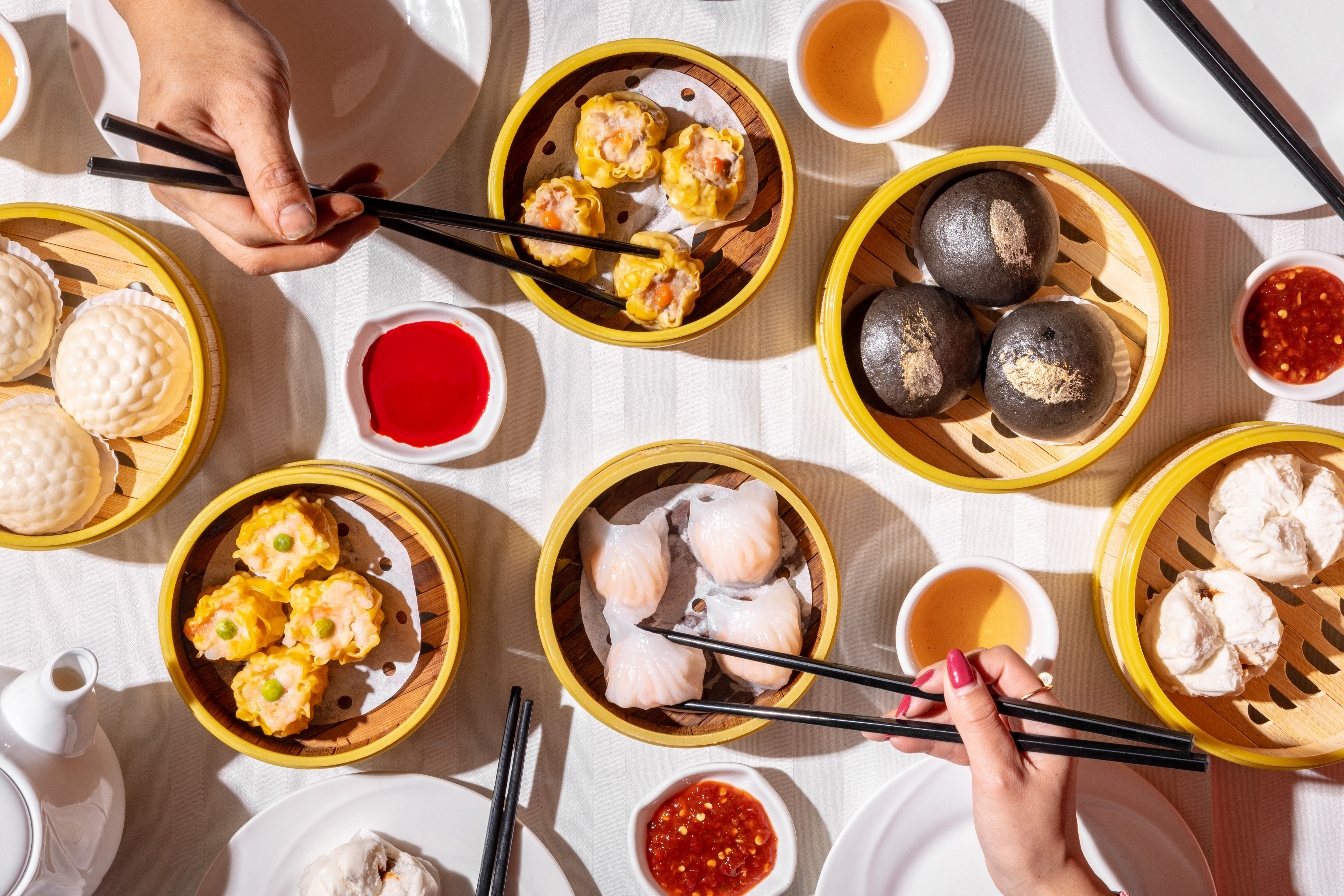 An overhead photograph of buns, siu mai, and other dim sum dishes in bamboo steamers.