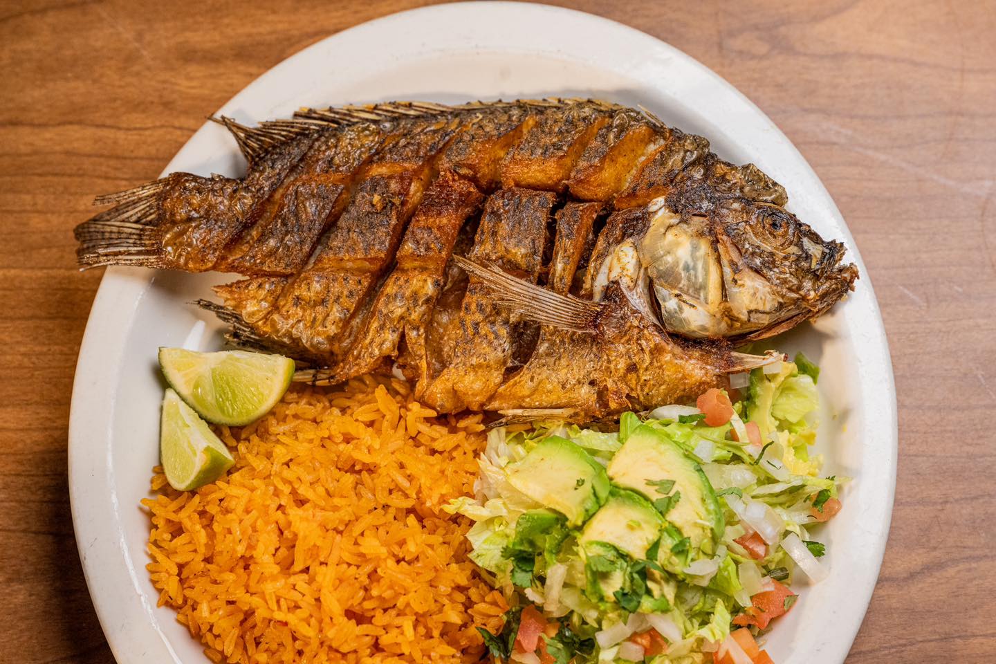 A fried whole fish served on a round white plate with red rice and salad from La Jalisciense Supermercado Y Taqueria in southwest Detroit, Michigan.