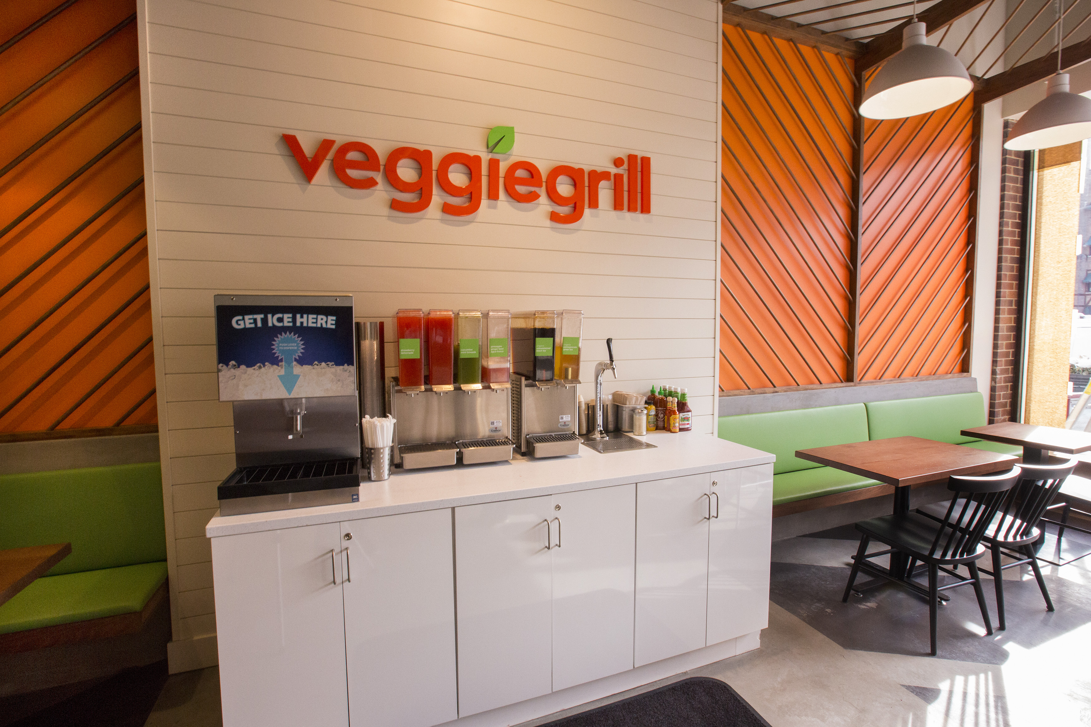 A wall with the words “Veggie Grill” in orange above a condiment stand.