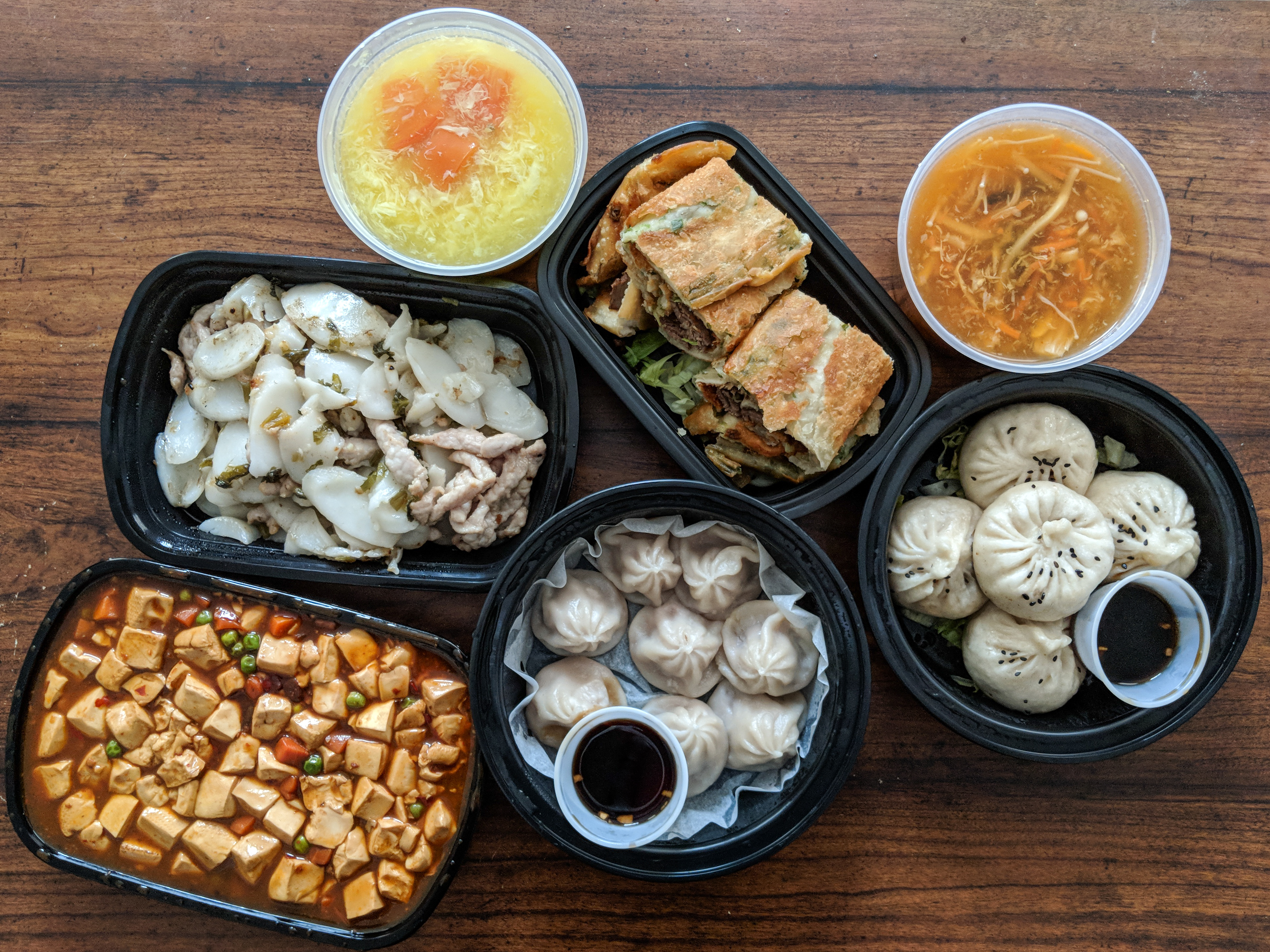 Dumpling Kitchen delivery spread, including mini juicy pork buns, roast beef with scallion pancake, ma po tofu, and more