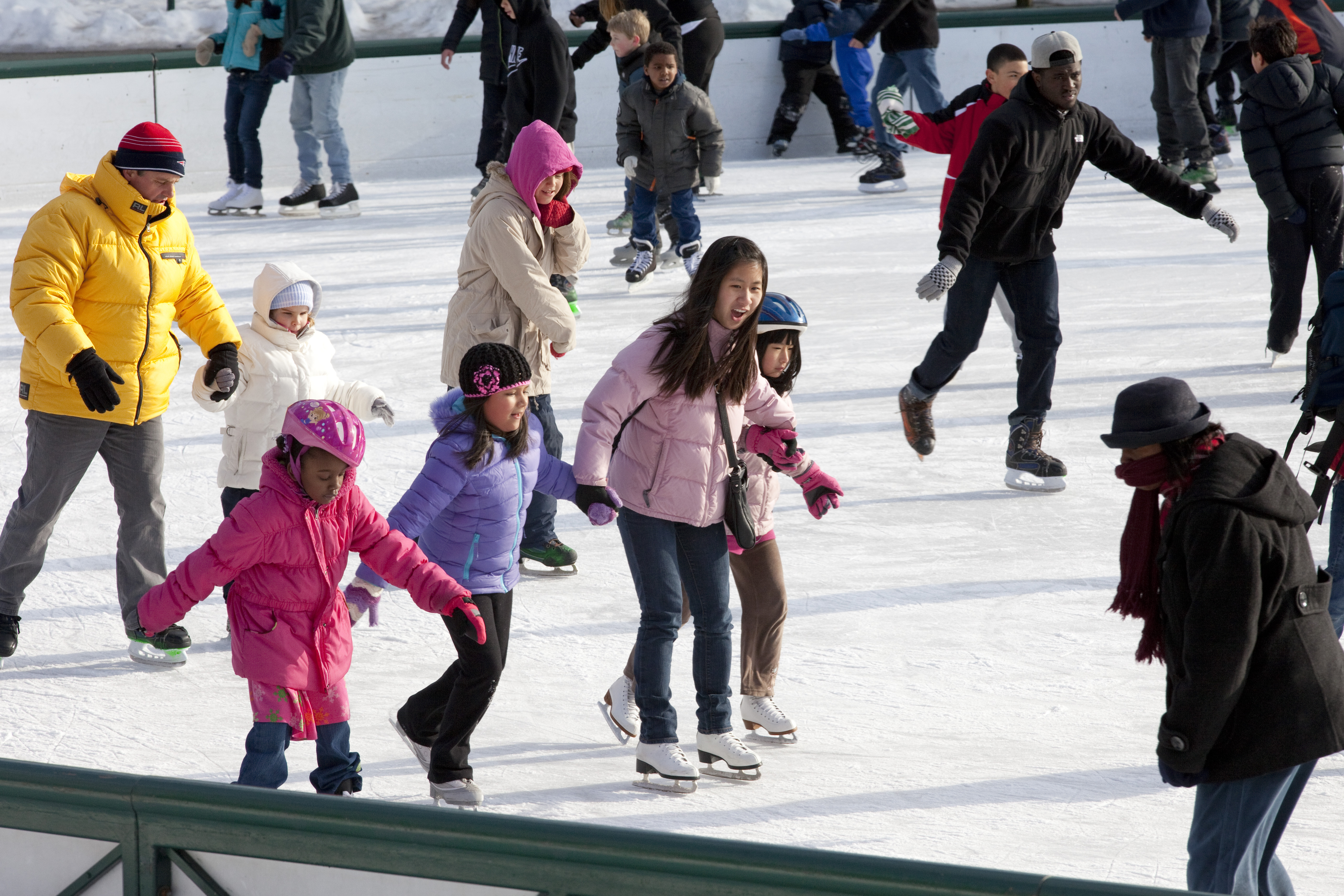 People joining hands and ice-skating on an outside rink.