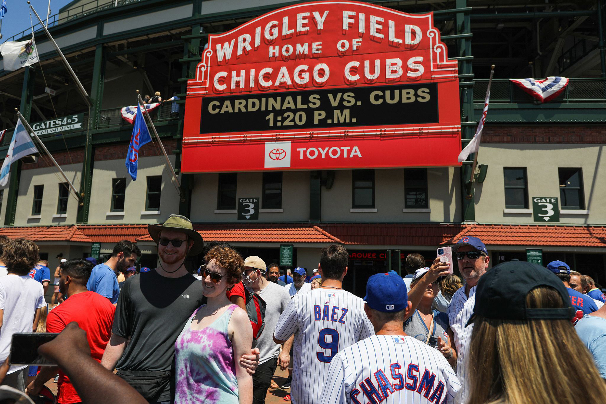 Fans walk toward the main entrance of a ballpark in Chicago with a big red sign.