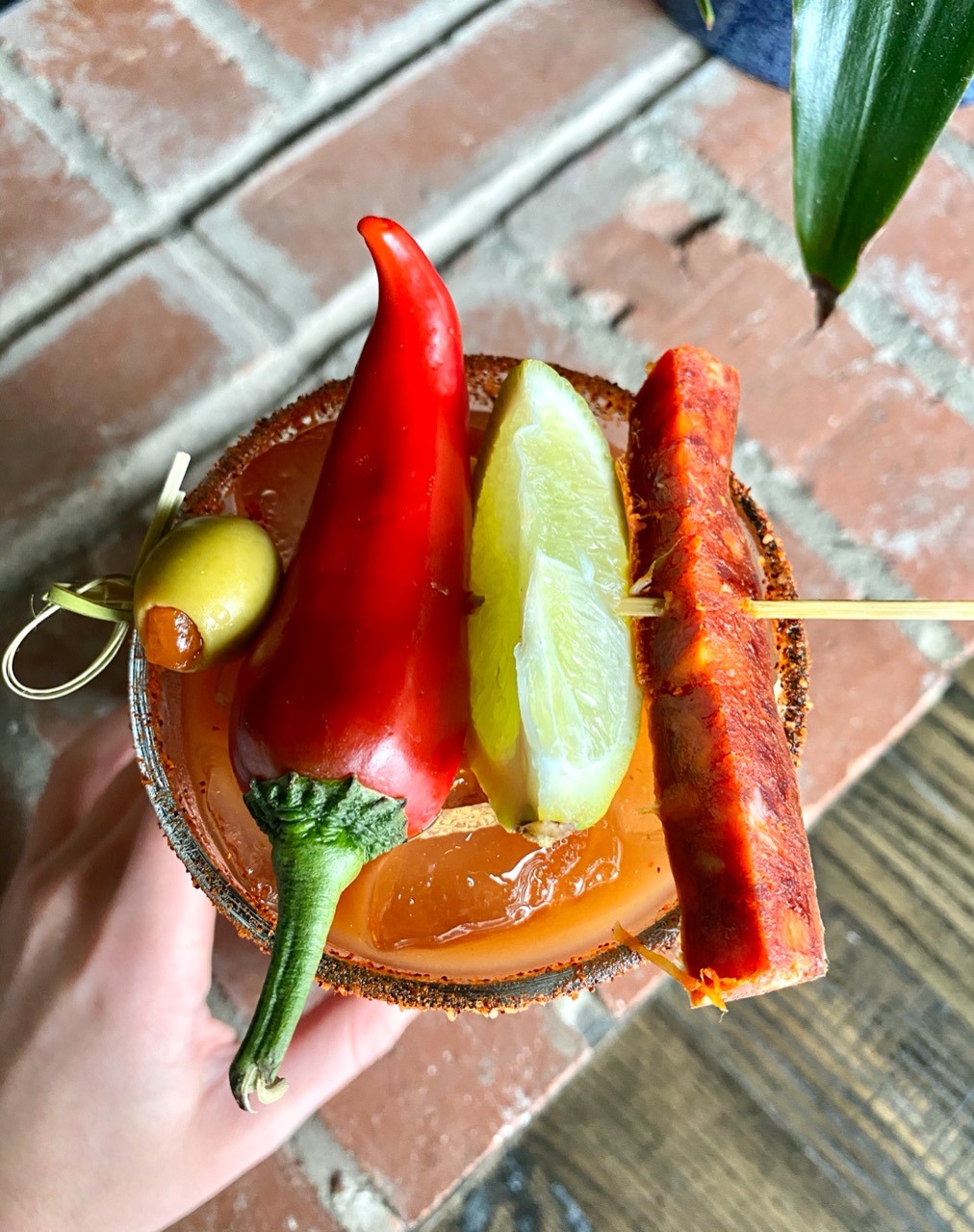 A bloody mary viewed from the top, garnished with lime wedge, olive, fresno pepper, and chorizo sausage