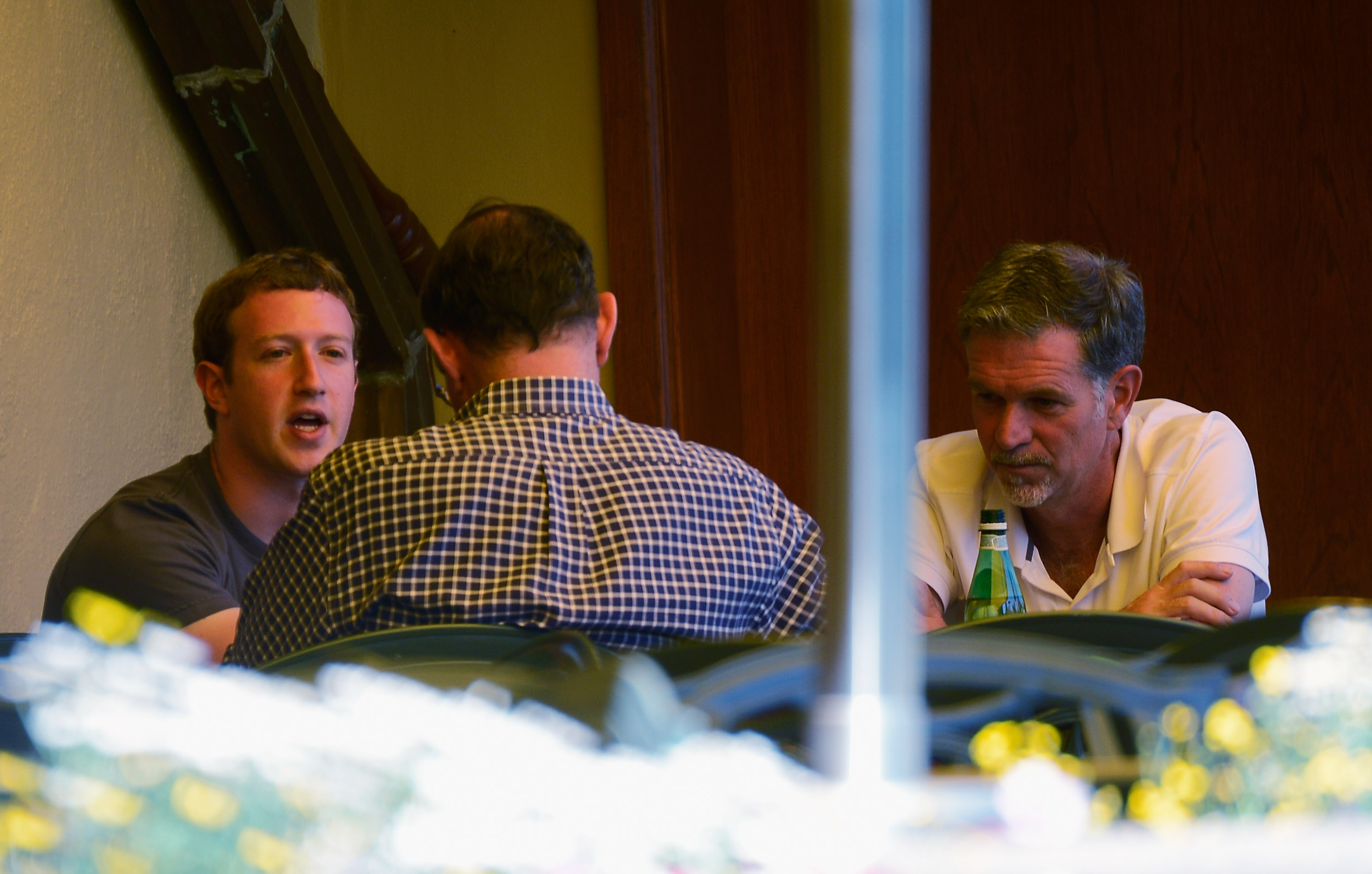 Facebook CEO Mark Zuckerberg and Netflix CEO Reed Hastings sitting at a table talking to a third person