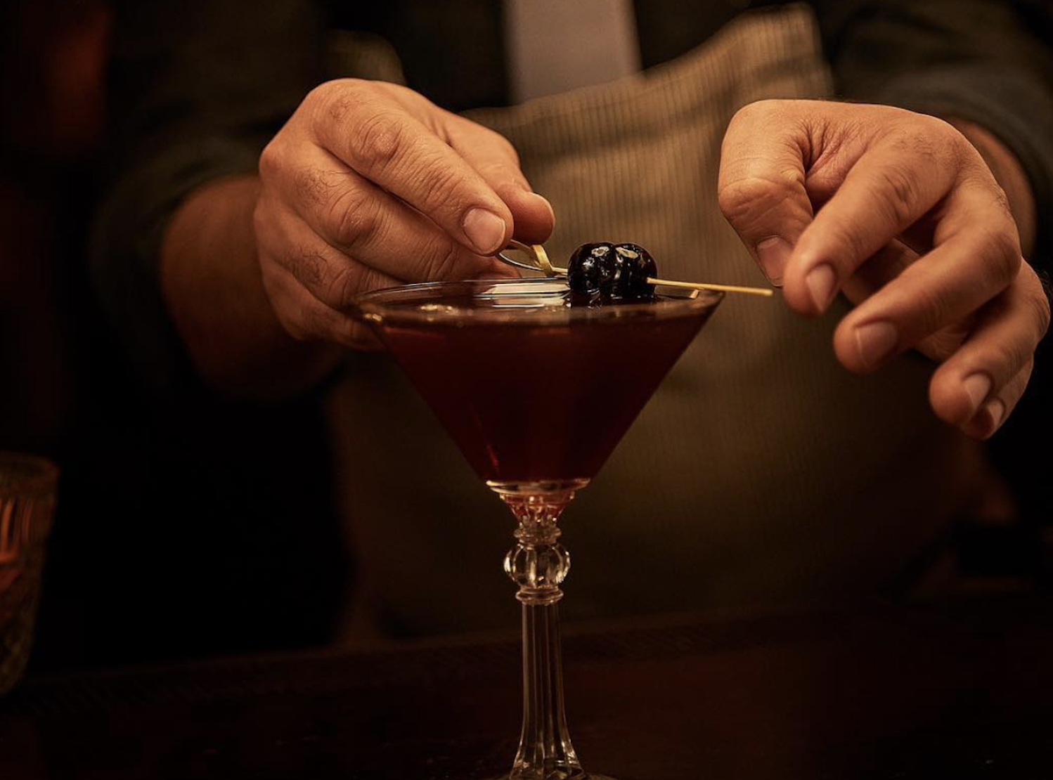 A pair of white hands serving a cocktail in a martini glass.