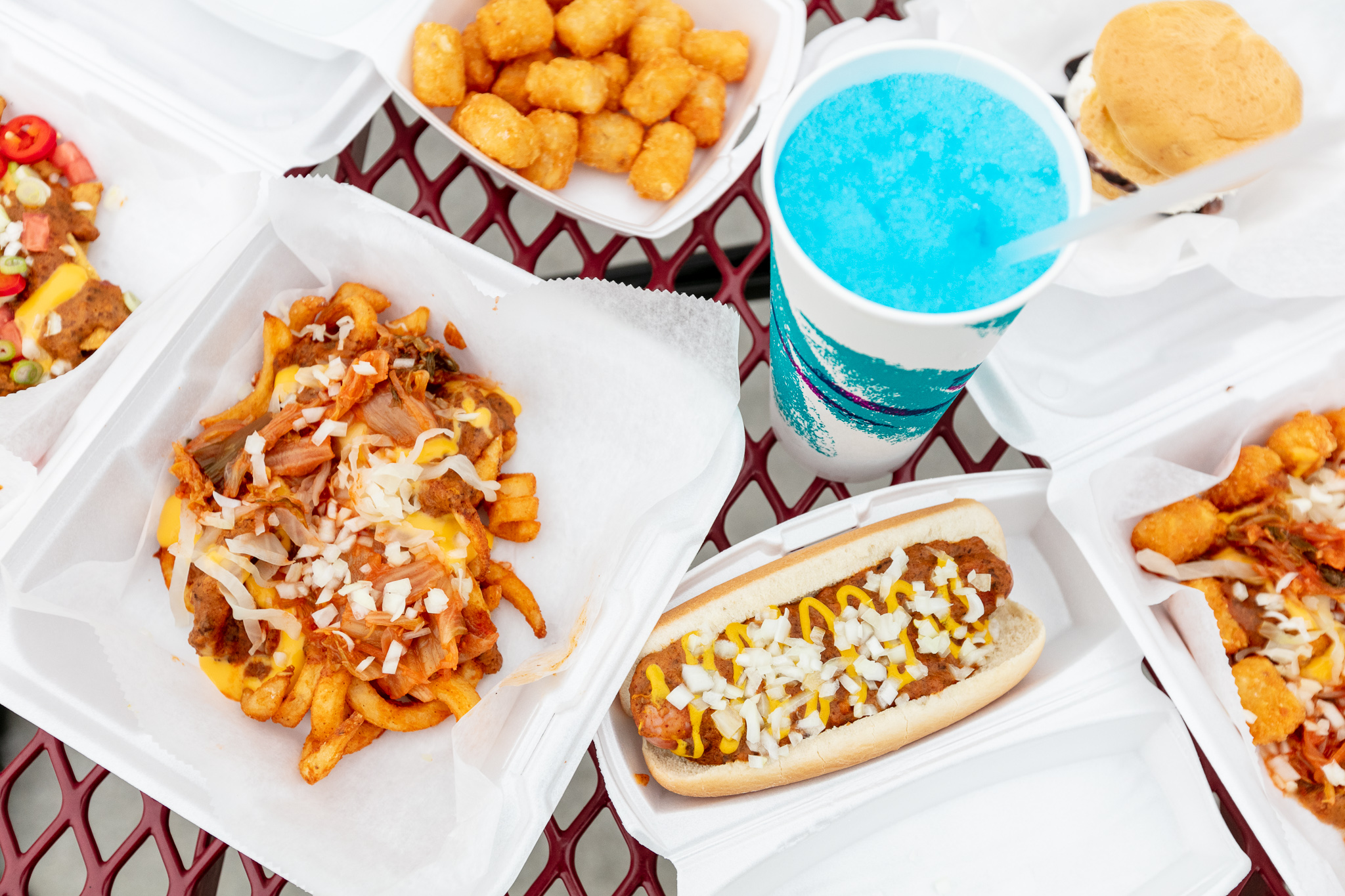 tater tots, a coney dog, curly fries covered in kimchi and onions, a cream puff, and a ‘90s-style paper cup with a blue drink inside