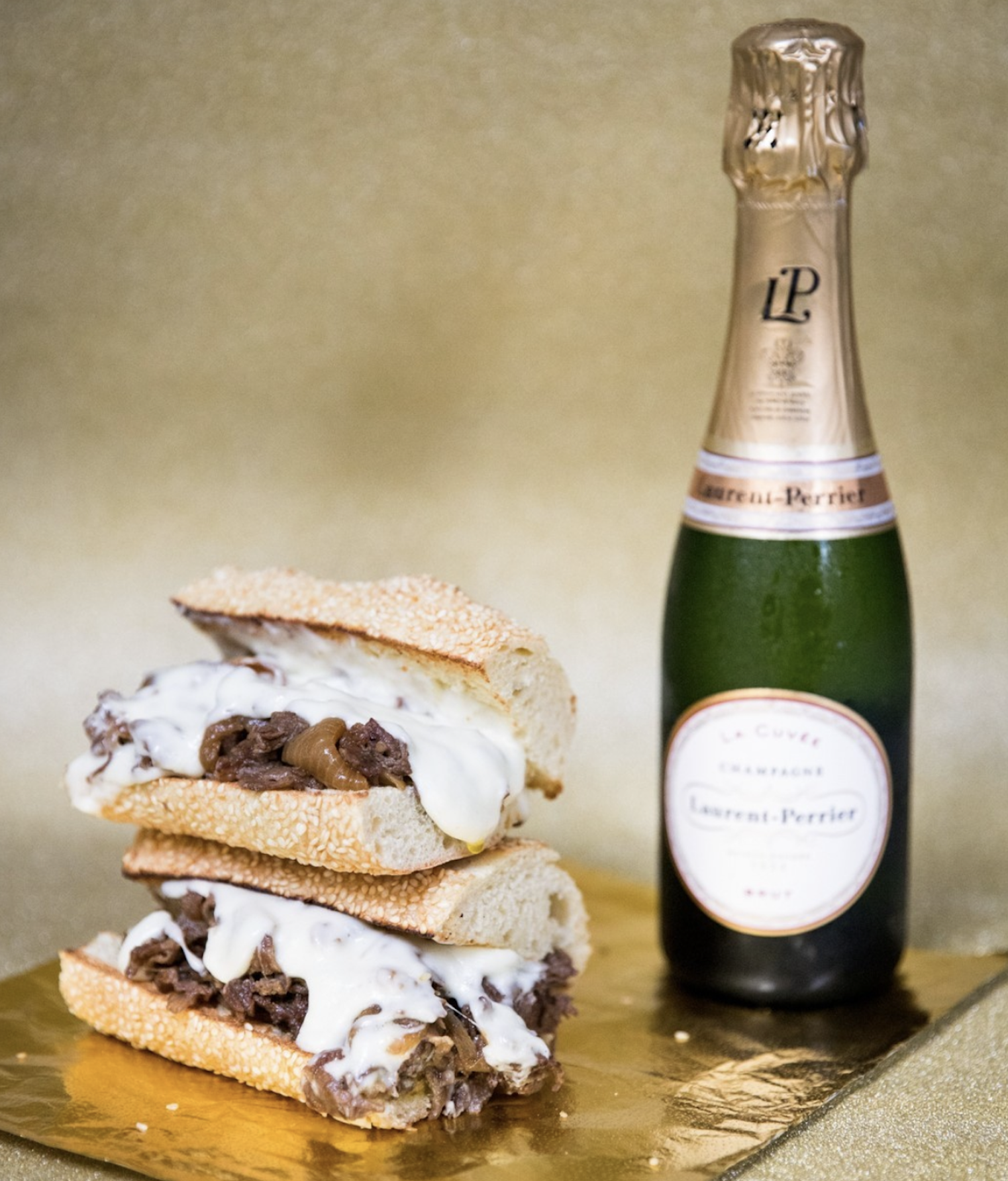 A cheesesteak sliced in two alongside a bottle of champagne. 