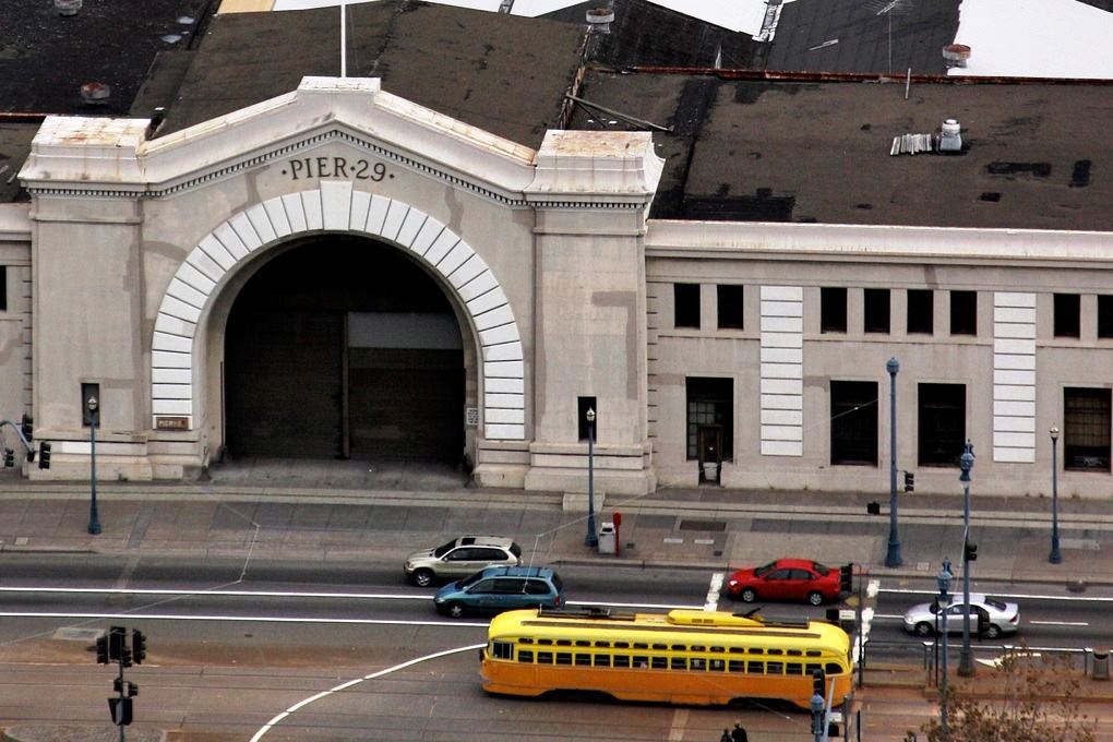 A yellow streetcar rolling by the bulkhead building at Pier 29.