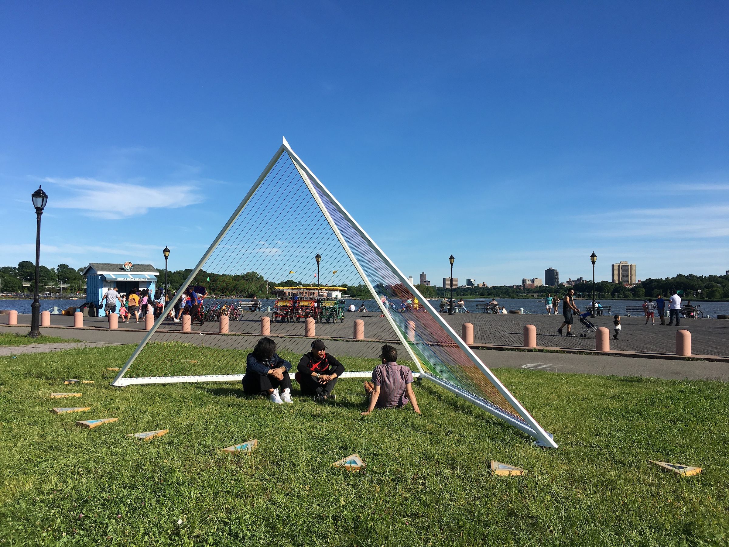 Three individuals under a triangular art installation in a park.