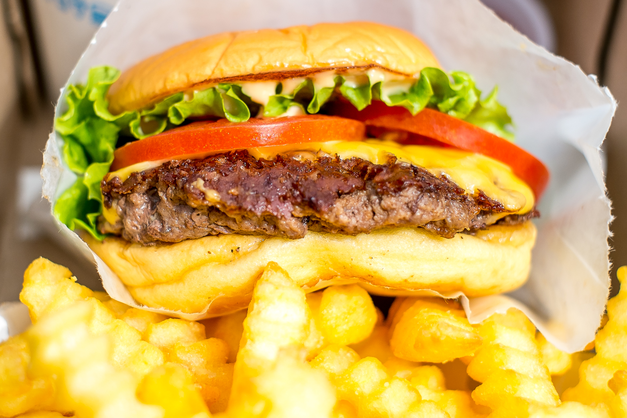 A Shake Shack burger in paper wrapping rests on top of crinkly fries.