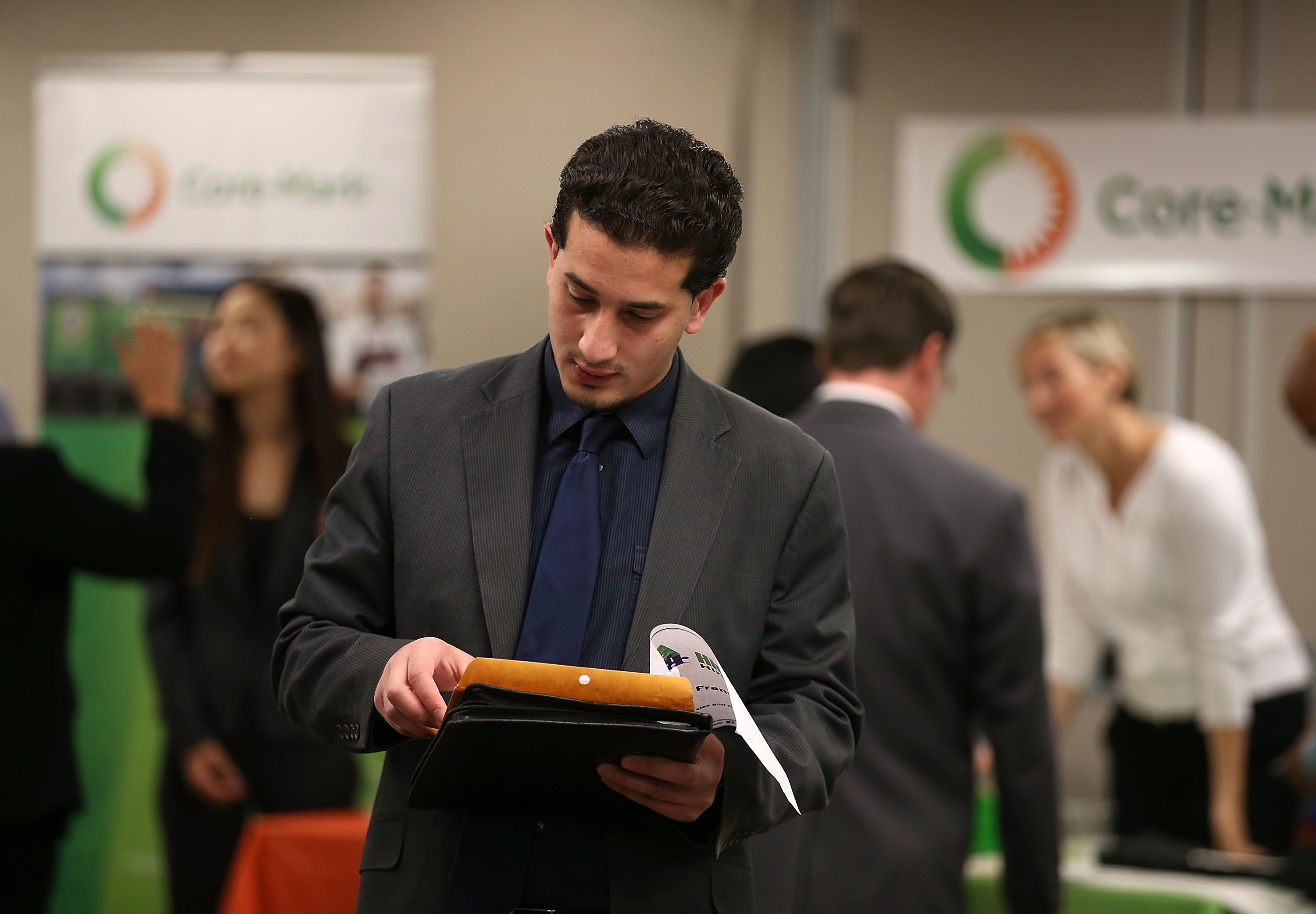 A young man looks at papers in his hand while he walks through a job fair