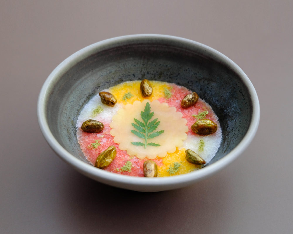 A bowl of brightly color granitas layered on one another with pistachios for garnish