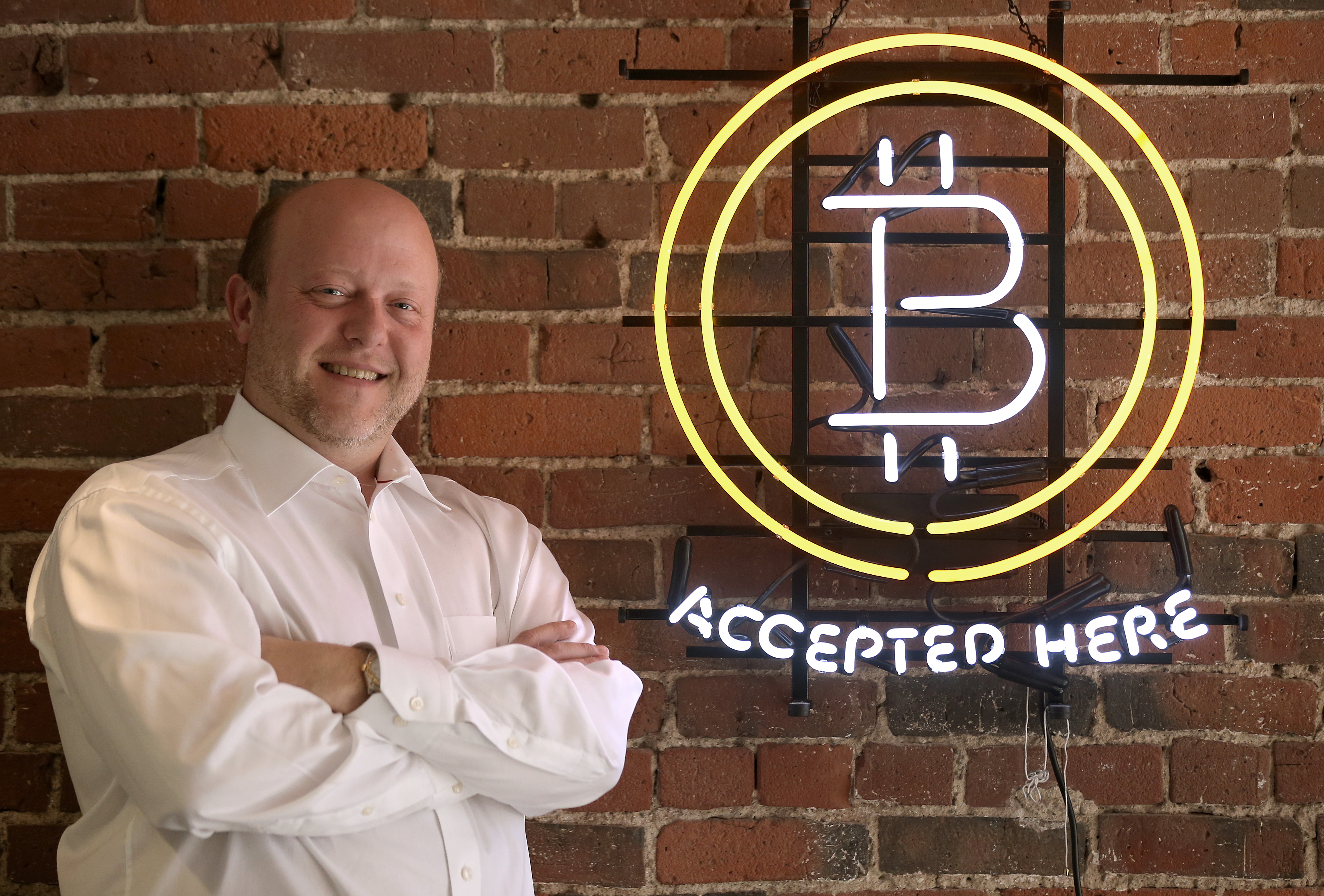 Circle CEO Jeremy Allaire stands next to a neon sign that reads “bitcoin accepted here.”