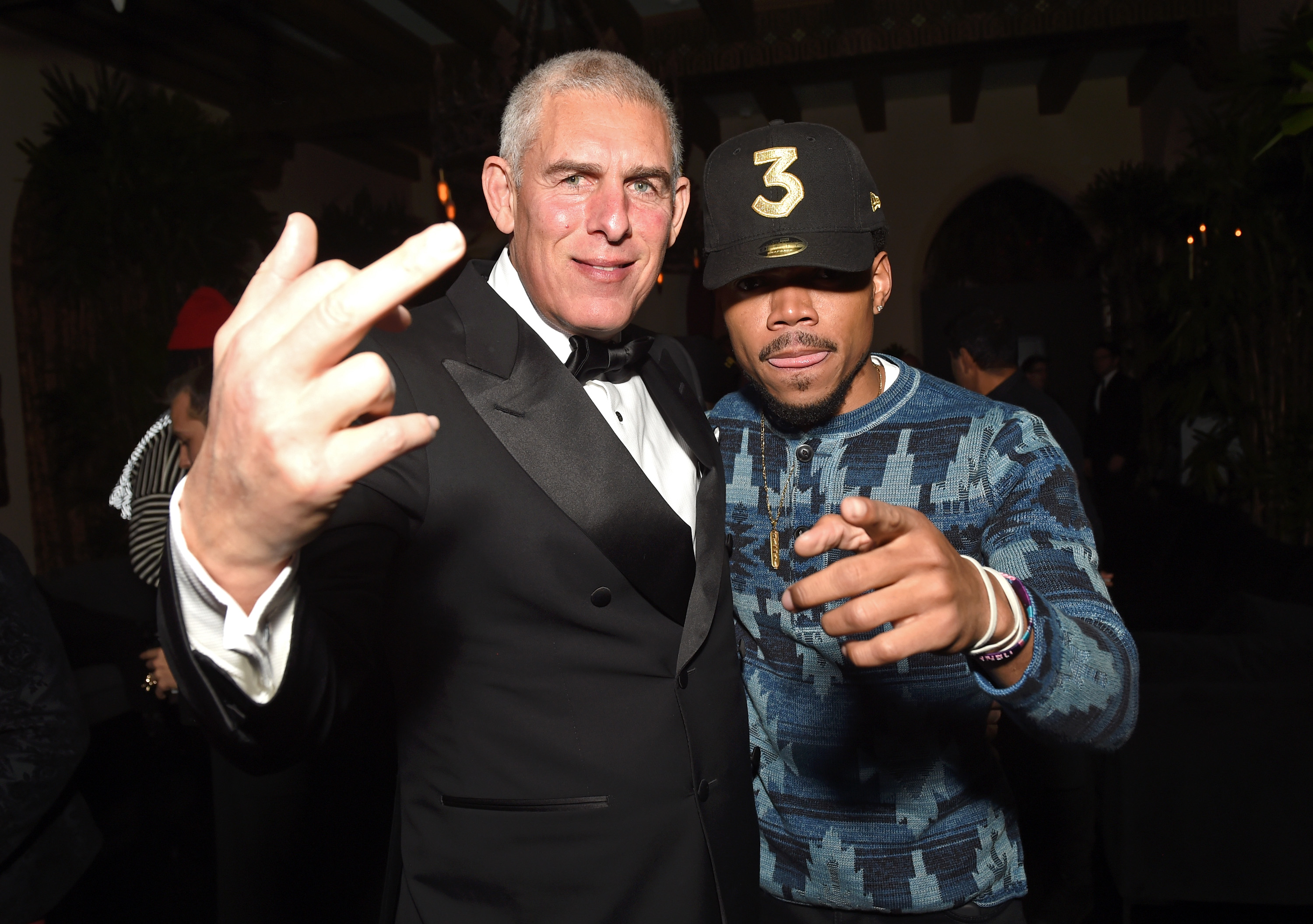 Youtube Head of Global Music Lyor Cohen raises his middle finger to the camera while standing beside Chance the Rapper, who points to the camera. 