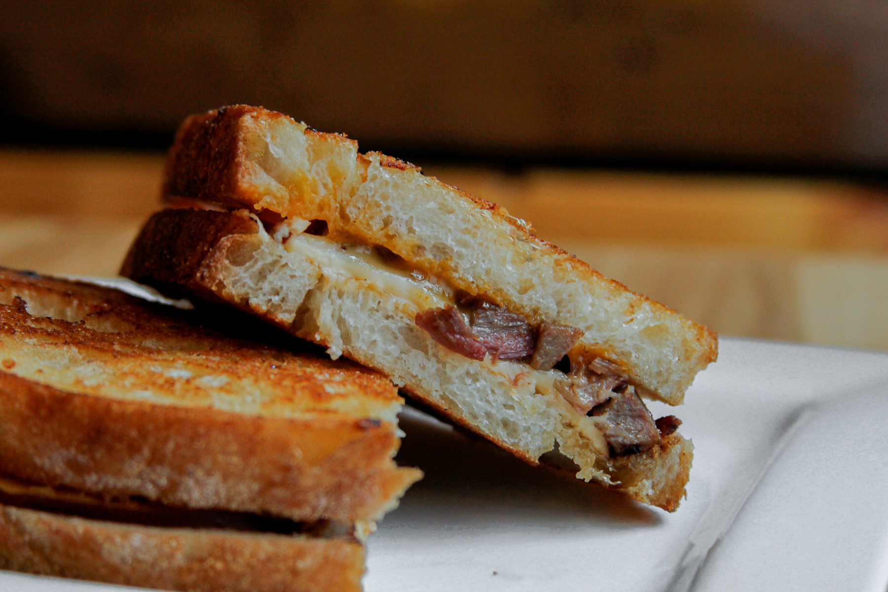 A grilled cheese sandwich with brisket sits on a white plate.