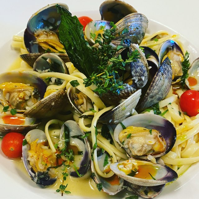 A plate of pasta and clams with cherry tomatoes and spices on a white plate.