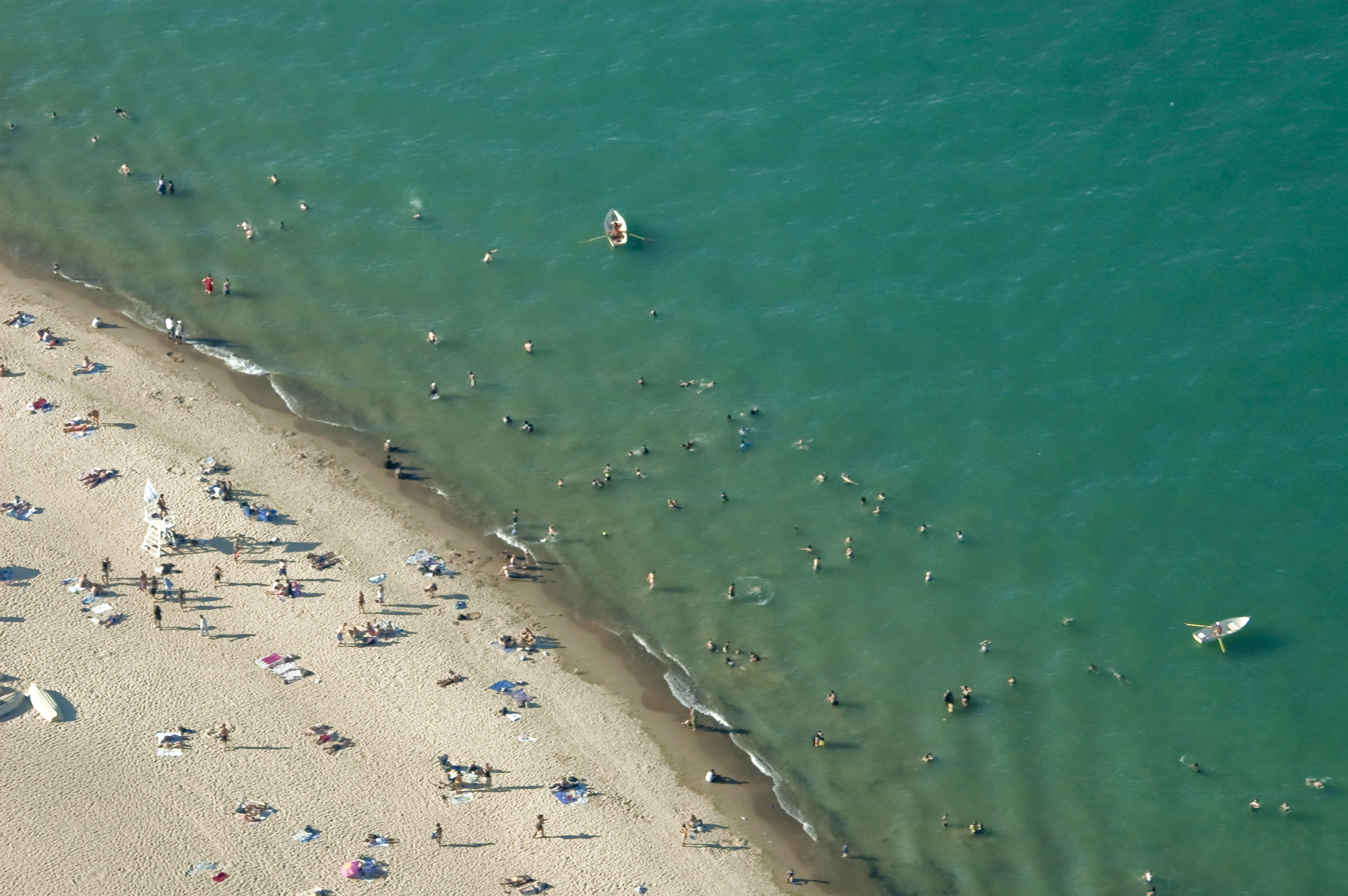 An aerial view of a beach with sand and the ocean. There are beachgoers in both the sand and ocean.