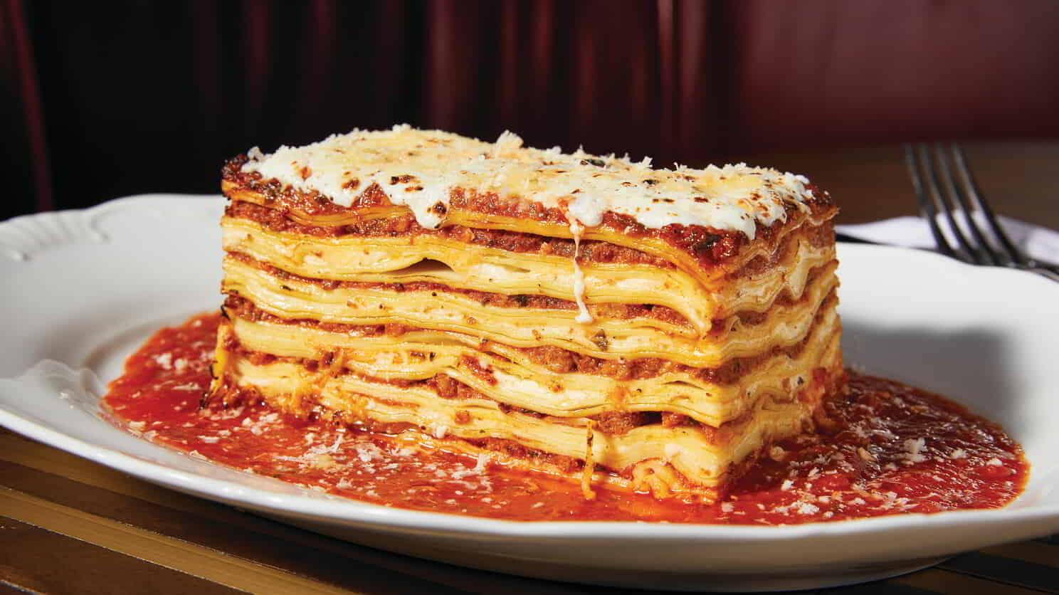 A tall lasagna topped with lots of cheese and sitting atop red sauce on a plate.