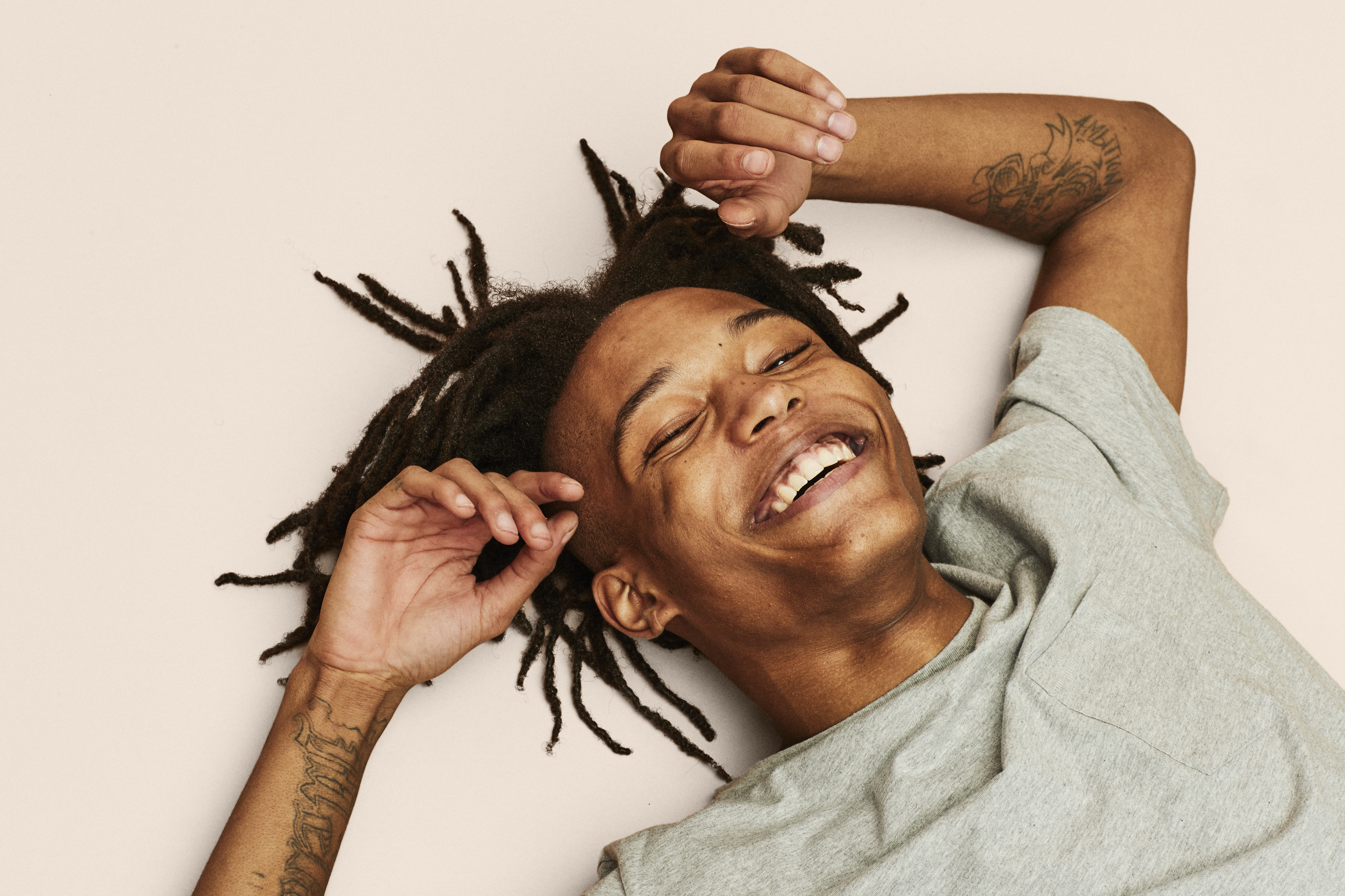 A smiling young man lies against a blush pink backdrop.
