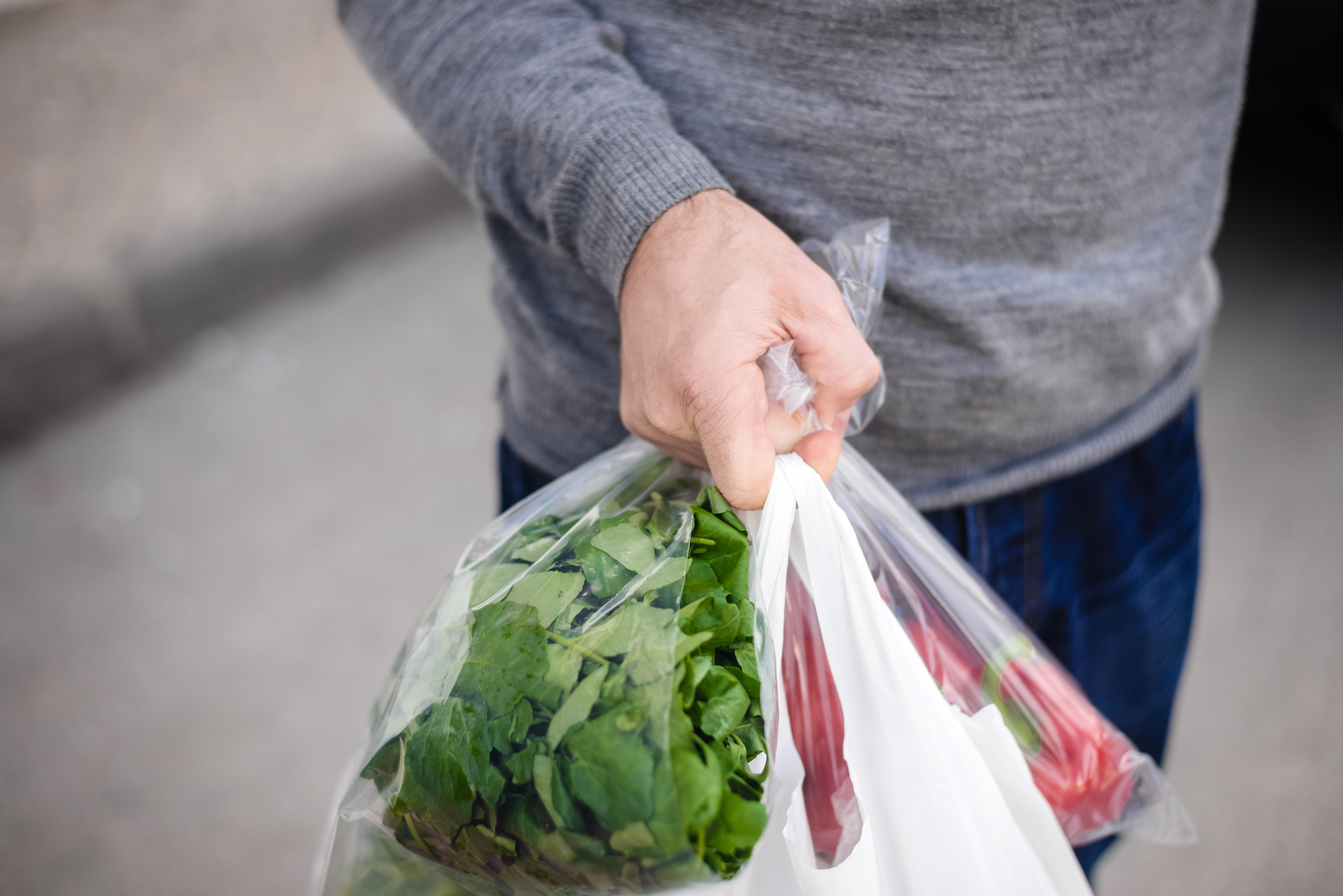 Man’s hand carrying plastic bags with vegetables in them
