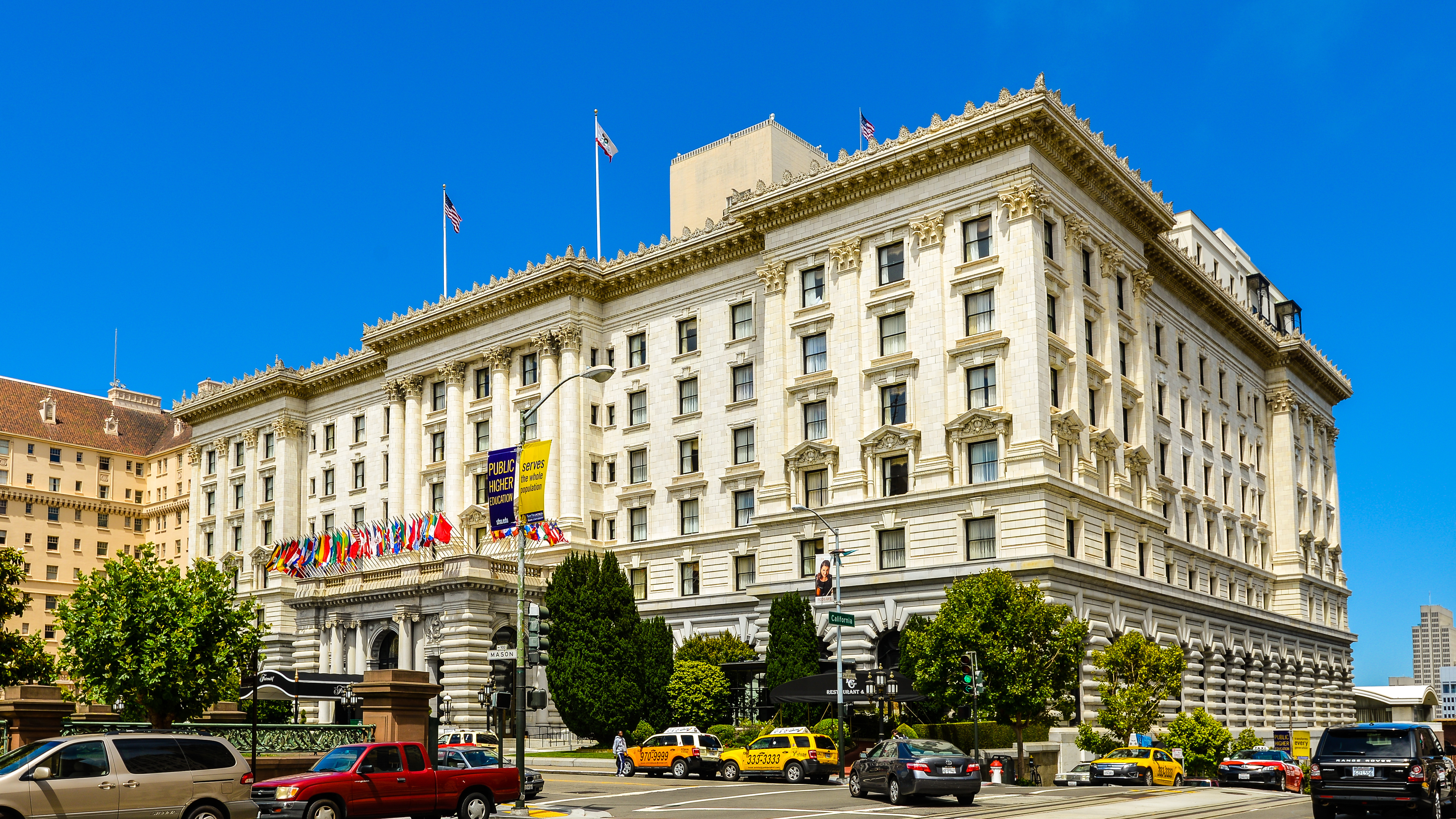 The exterior of a hotel in San Francisco. The facade is white with multiple windows and trees in front.