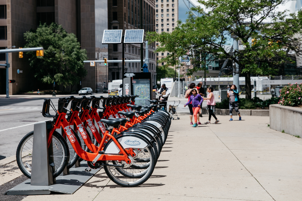 A row of red frame bikes locked at in a metal station on a downtown sidewalk.
