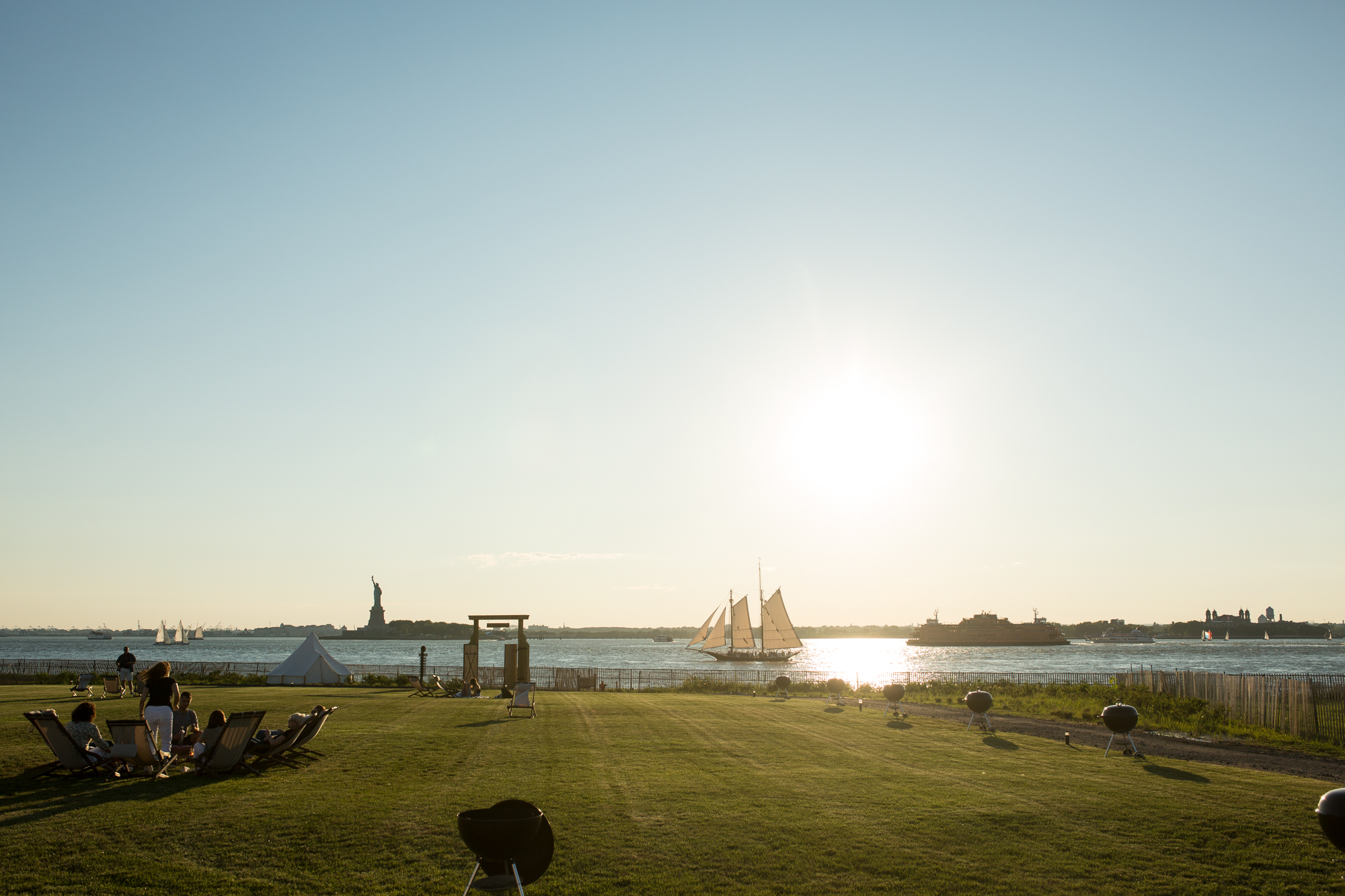 A lawn is in the foreground. In the distance is a body of water and the monument called the Statue of Liberty.