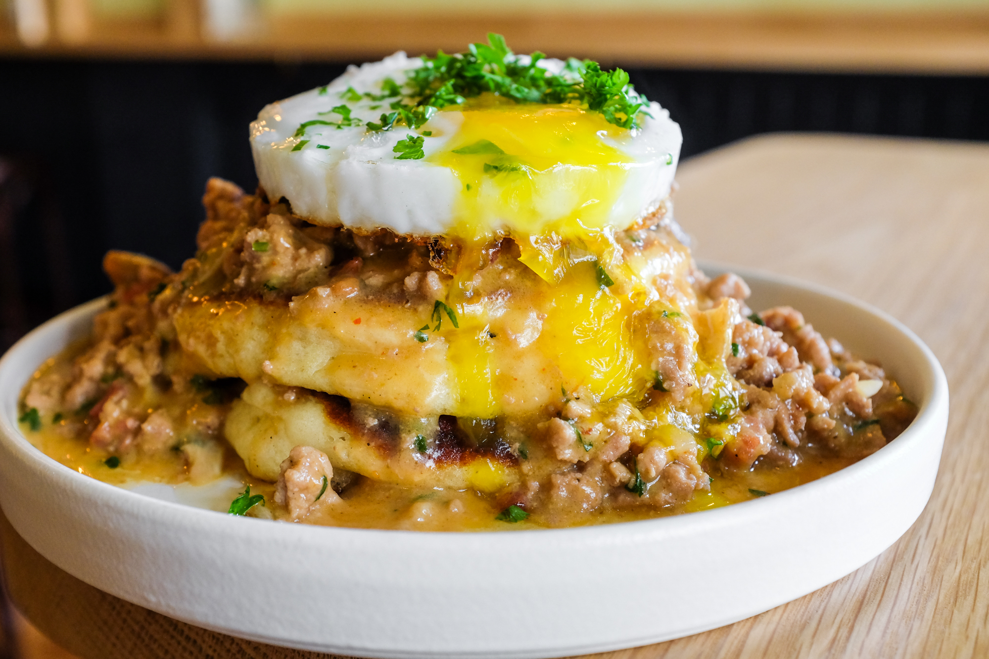 A duck egg is perched on a stack of pancakes at Canard, drizzled with duck sausage gravy and chopped herbs.