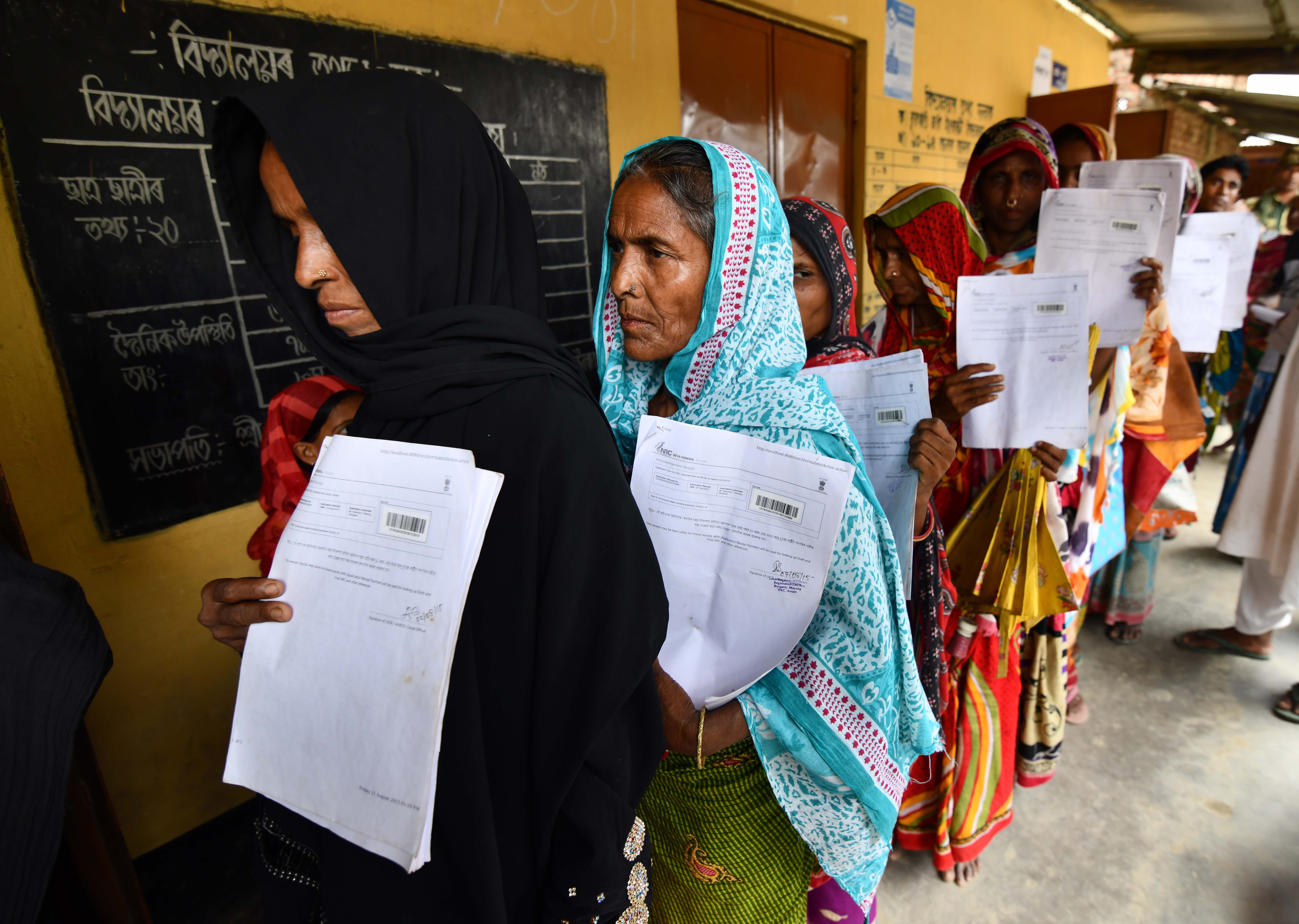 Indian women wrapped in scarves hold their documents as they stand in line to check their names on the National Register of Citizens.
