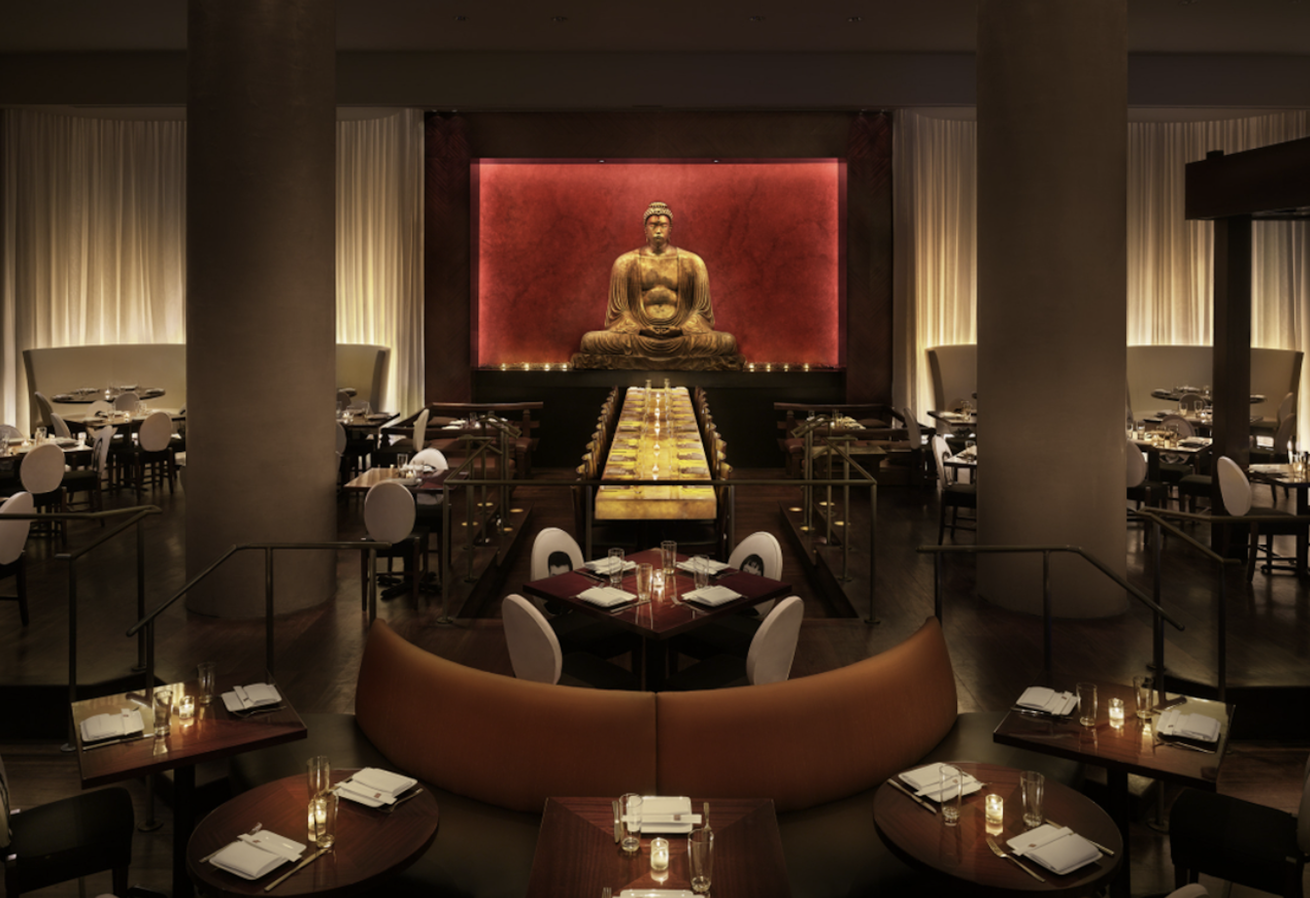 A wide shot of a dimly lit dining room with a golden statue of Buddha in the center. 