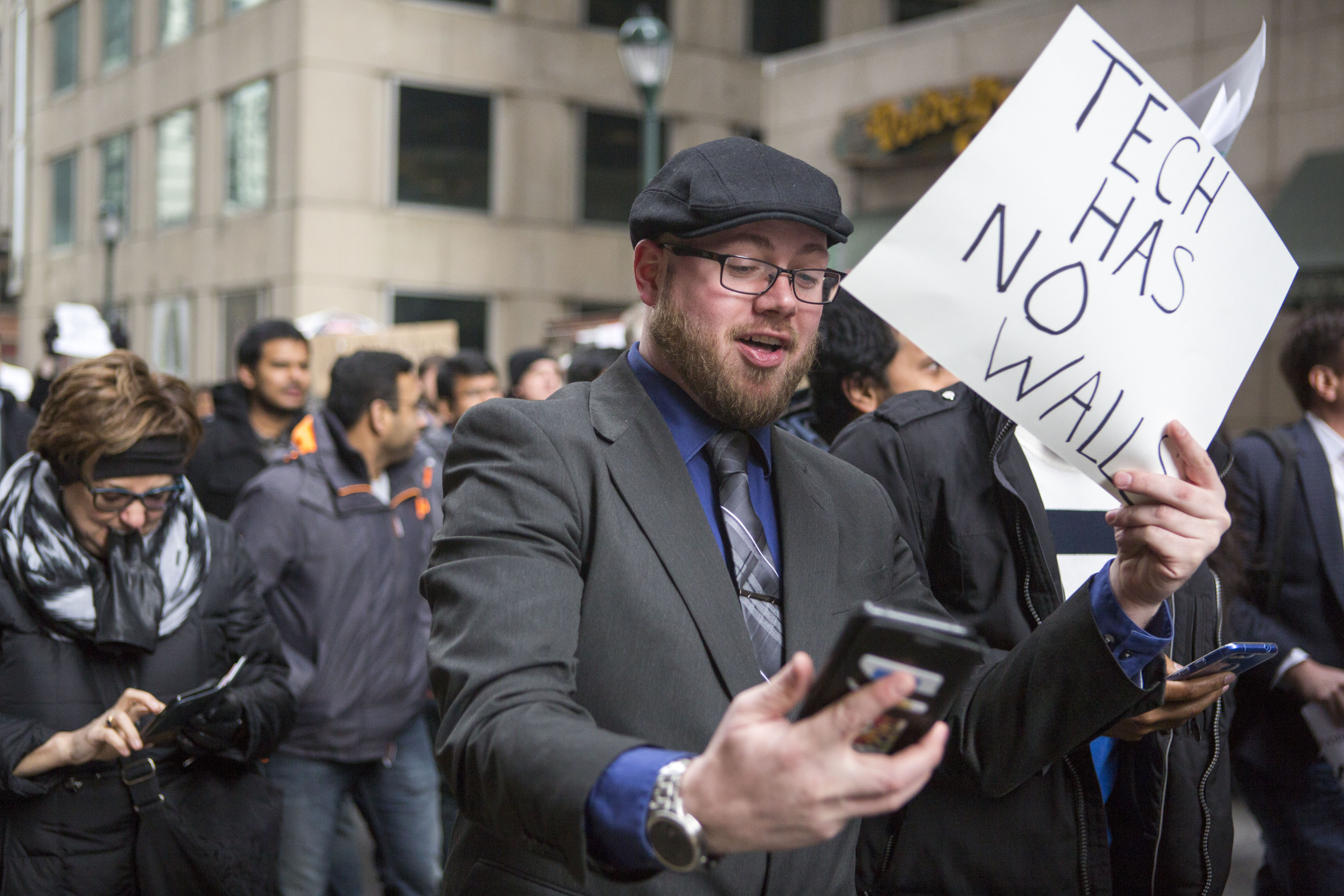 A man marching in a protest holds a sign reading “Tech has no walls”