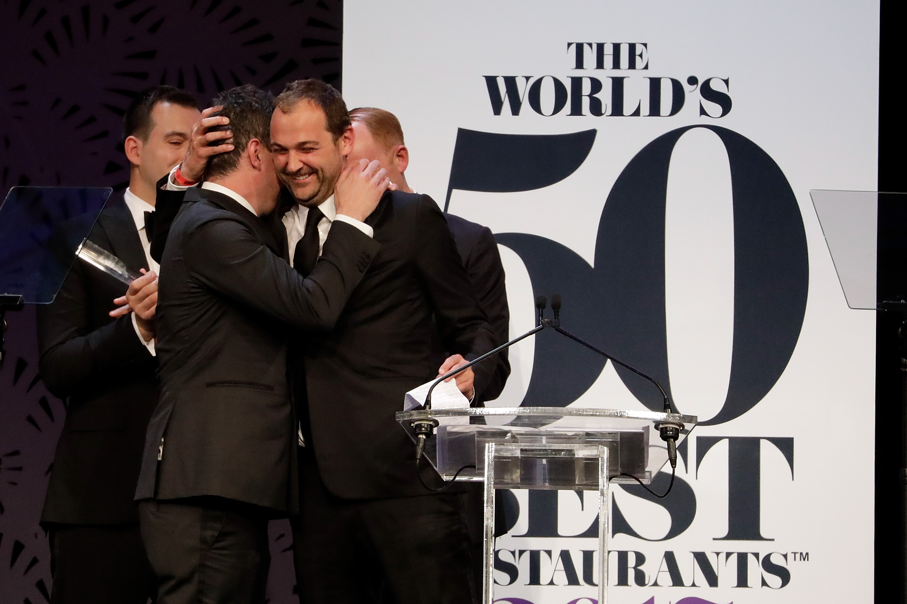 Will Guidara and Daniel Humm embrace on stage in front of a World’s 50 Best Restaurants banner.