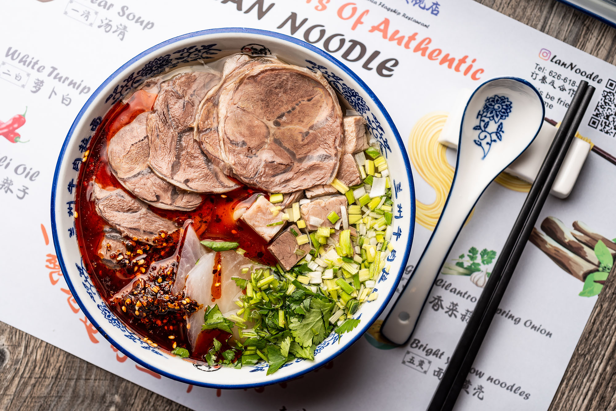 A bowl of Lanzhou beef noodle soup with meat and chile oil.