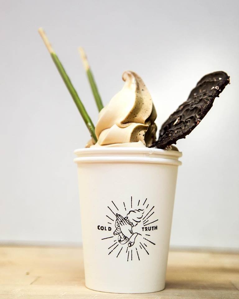 a white cup with a chocolate vanilla swirl of soft serve. It has two green matcha flavored Pocky sticks poking out of the top as well as a chocolate covered potato chip