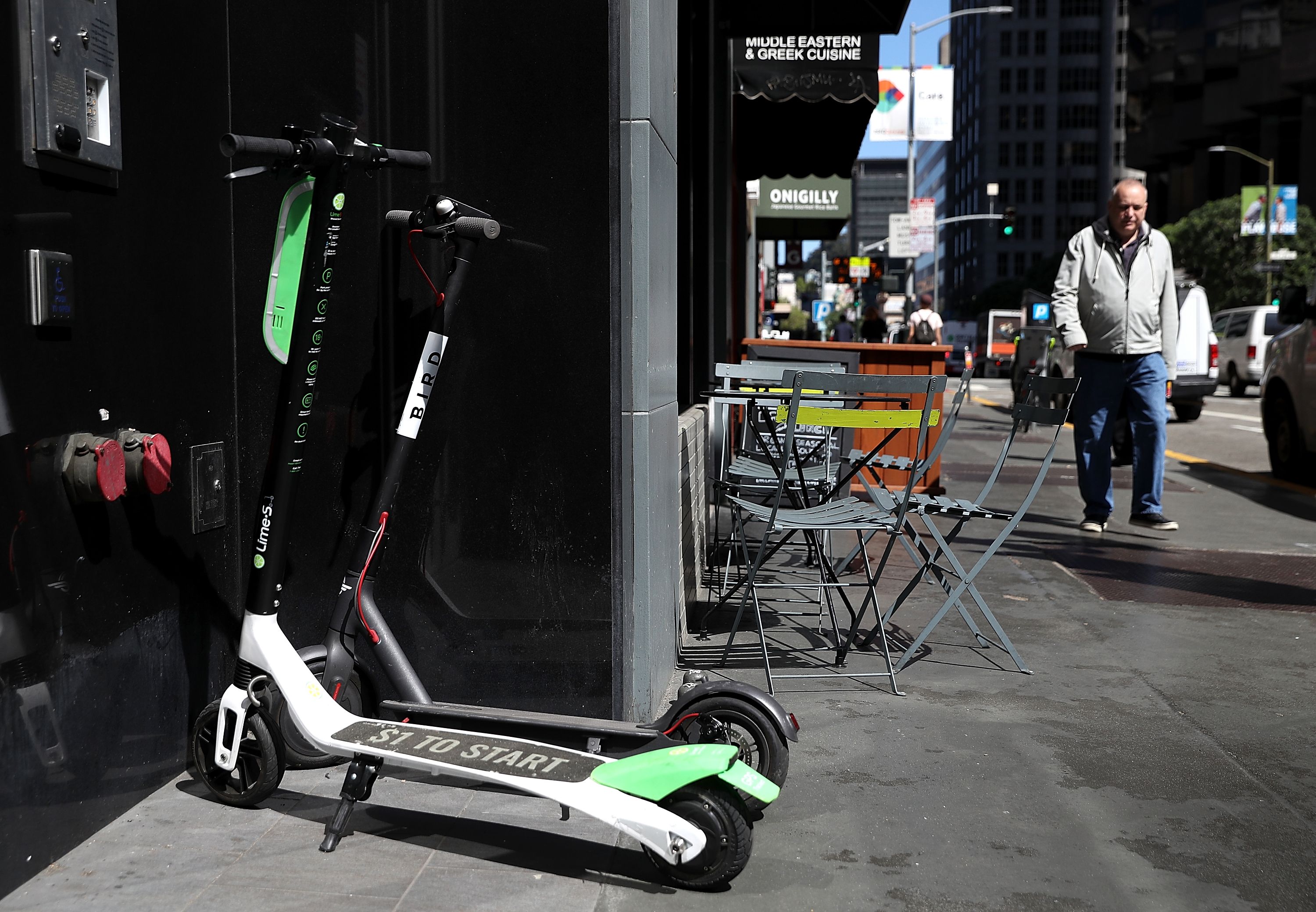 Green and white Lime scooters parked on the sidewalk. A male pedestrian walks near them.