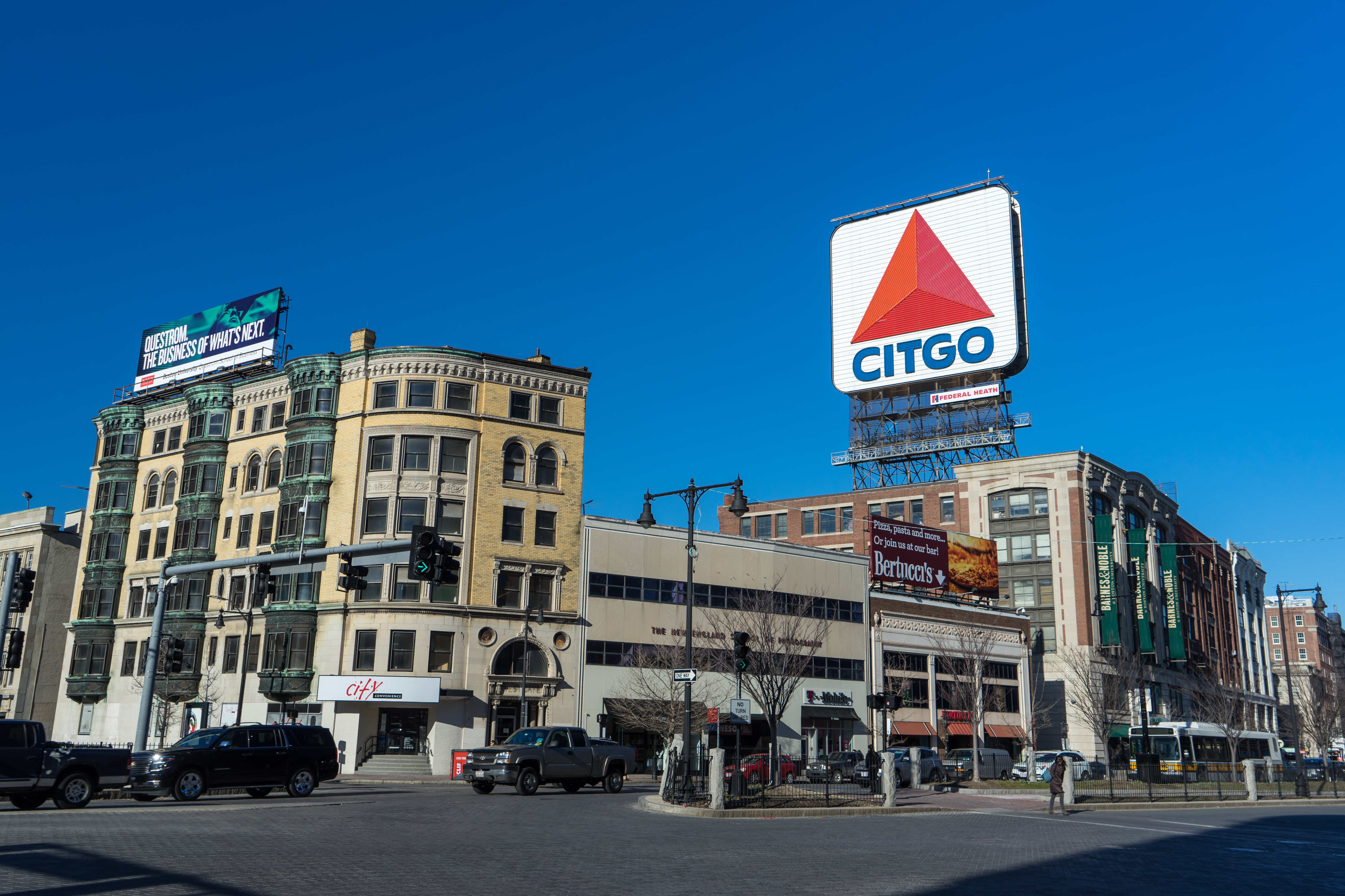 A row of various city buildings on a block in Boston. Above one of the buildings is a sign that reads: Citgo. There is a street in front of the buildings with cars.