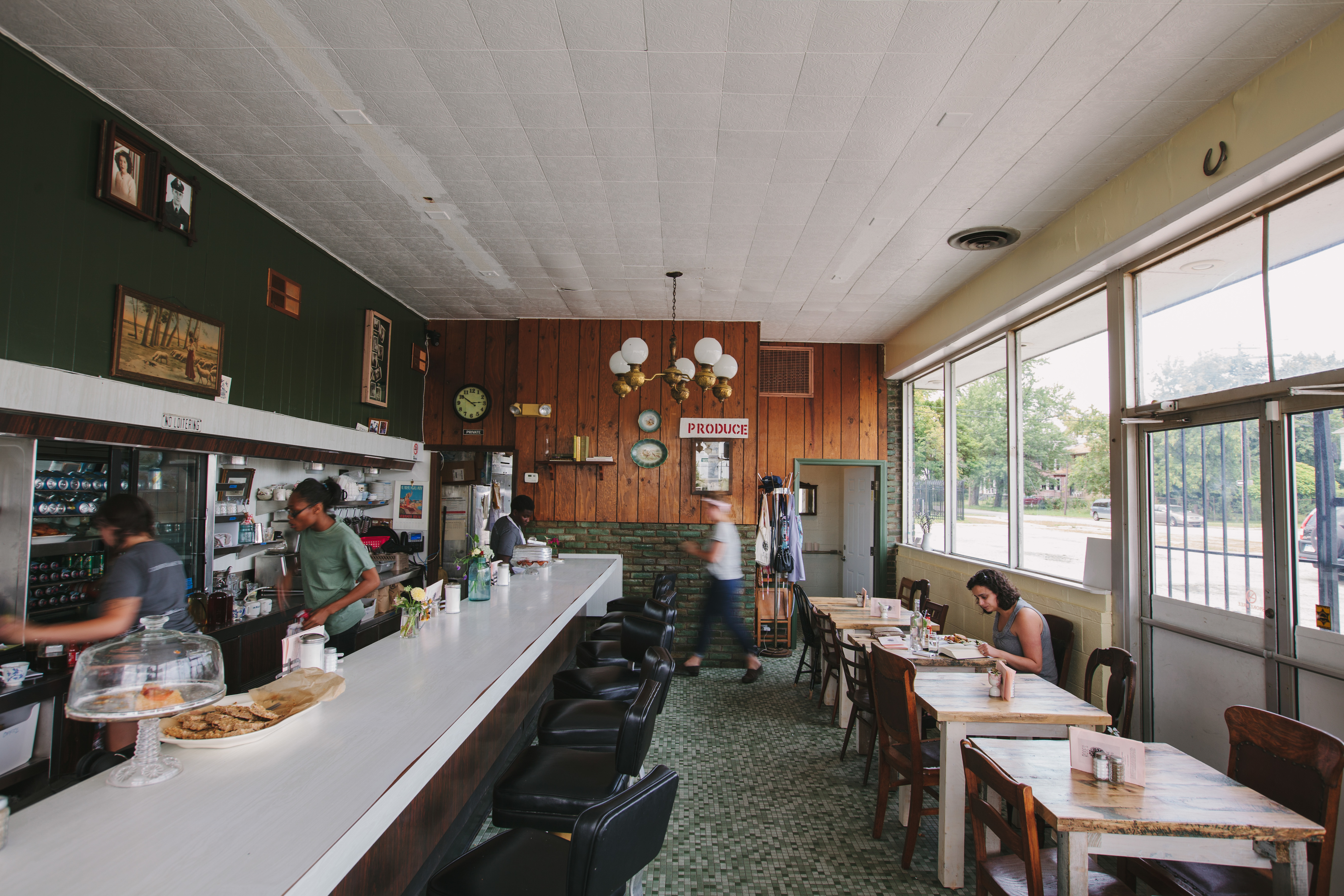 A green and wood-paneled diner restaurant with a lunch counter and kitchen staff standing behind the bar.