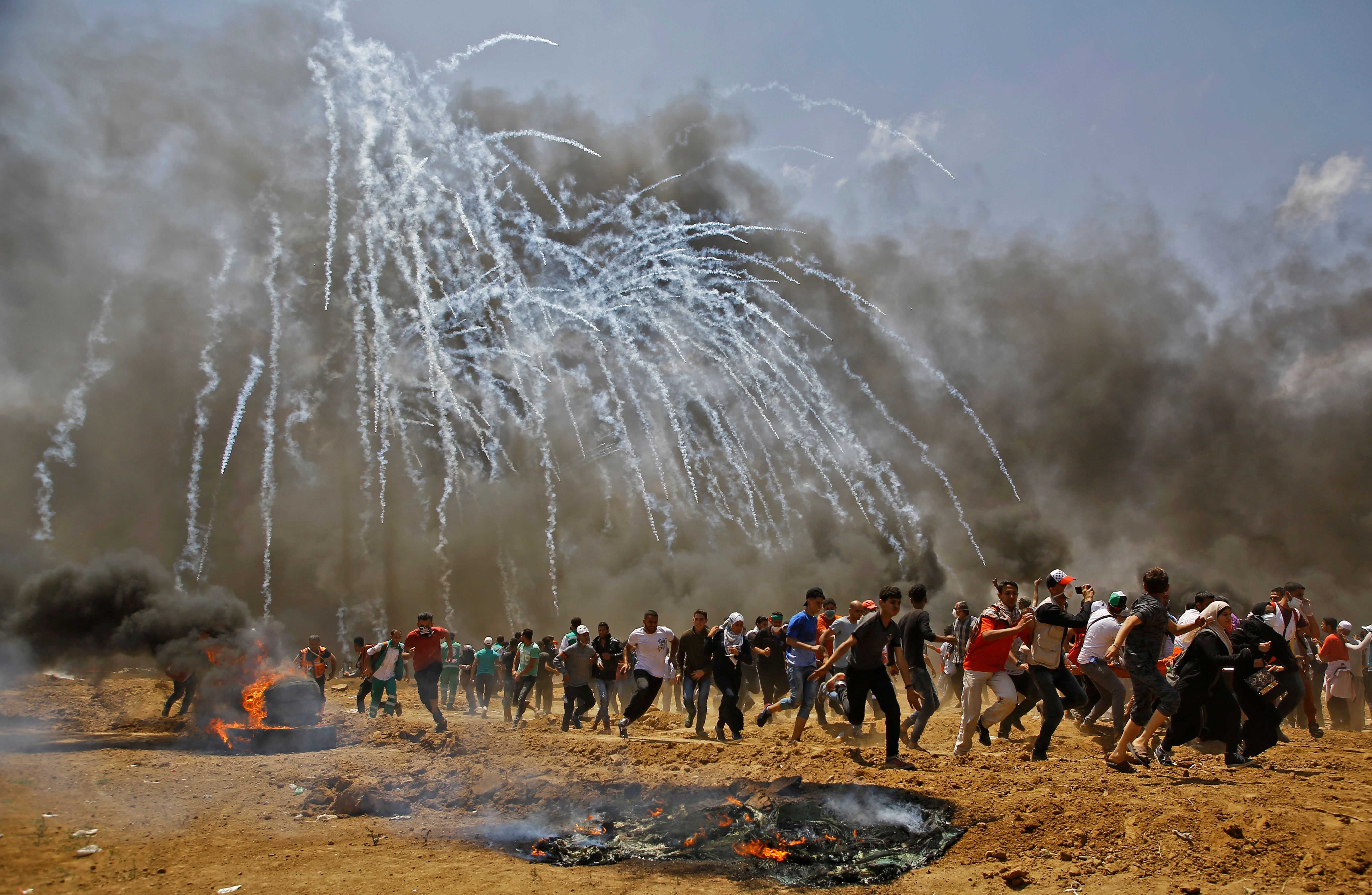 Palestinians run for cover from tear gas during clashes with Israeli security forces near the border between Israel and the Gaza Strip, east of Jabalia on May 14, 2018.
