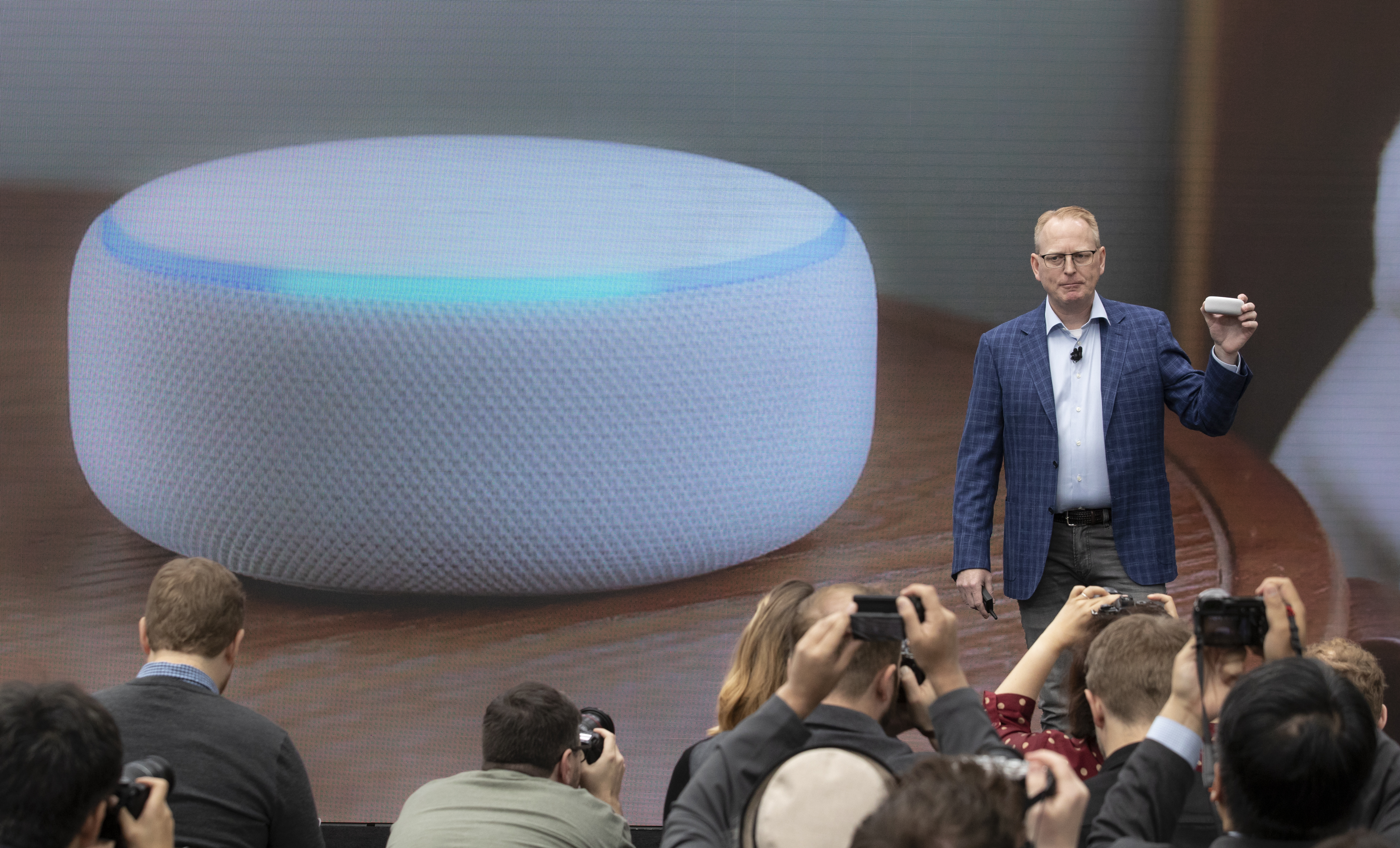 Dave Limp, Senior Vice President of Amazon Devices, stands onstage in front of a picture of a redesigned echo dot device.