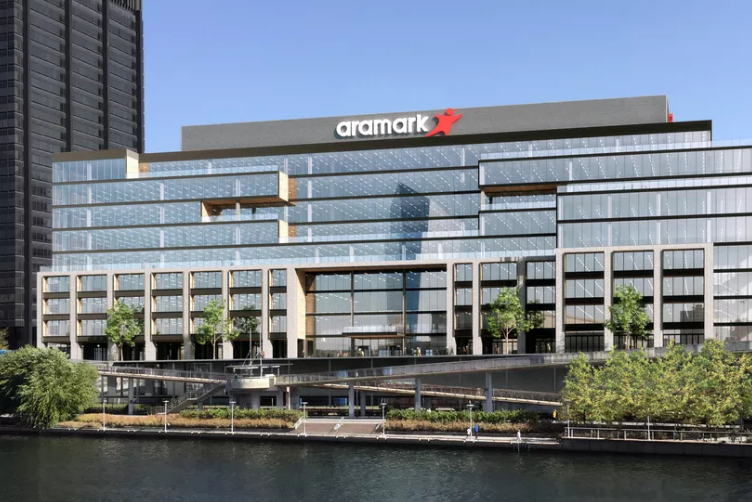 The exterior of 2400 Market Street in Philadelphia. The facade is glass. There are trees in front and a body of water. There is a sign on the building that reads: Aramark.