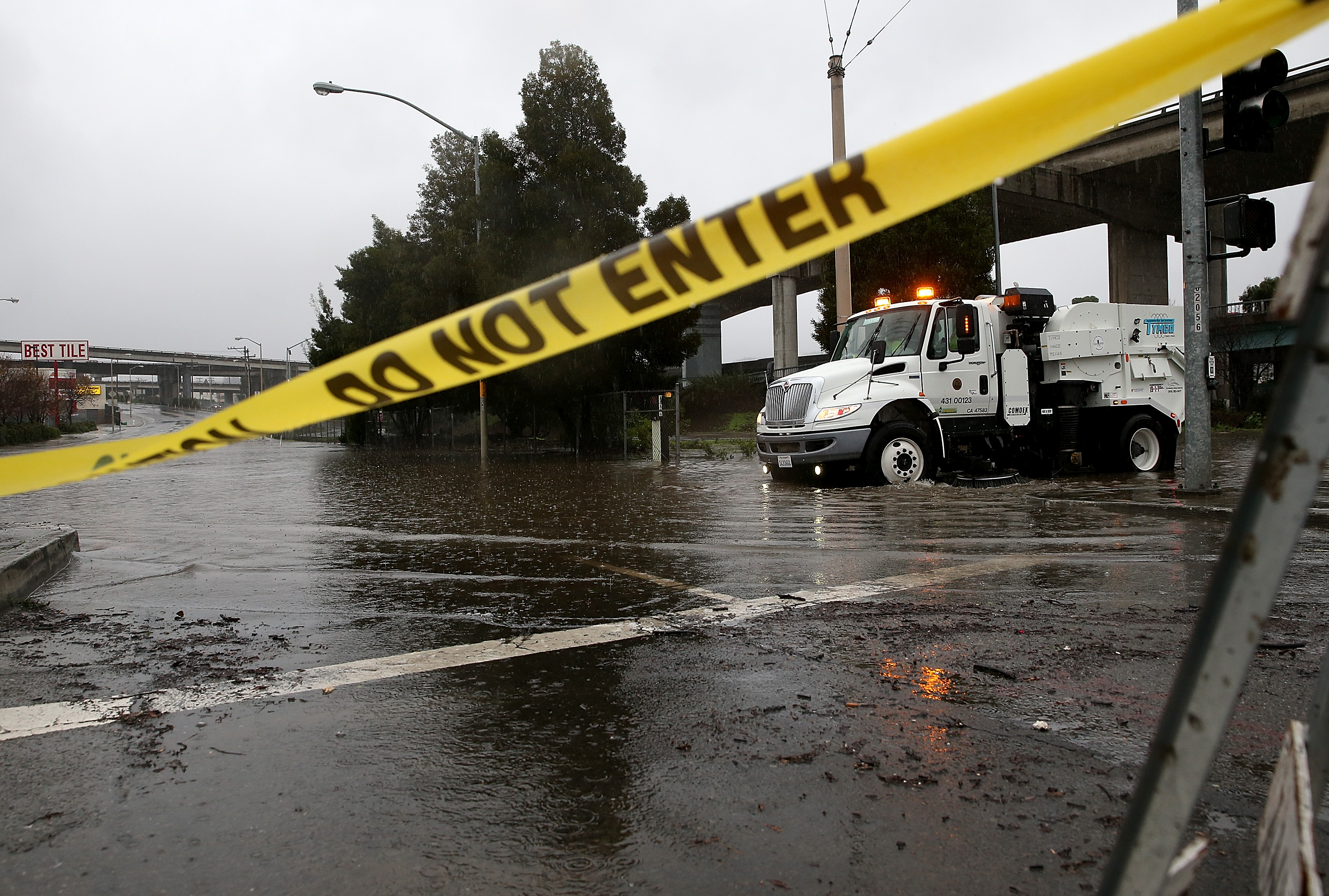 A San Francisco Department of Public Works street cleaner attempts to clear a drain that is causing an intersection to flood.