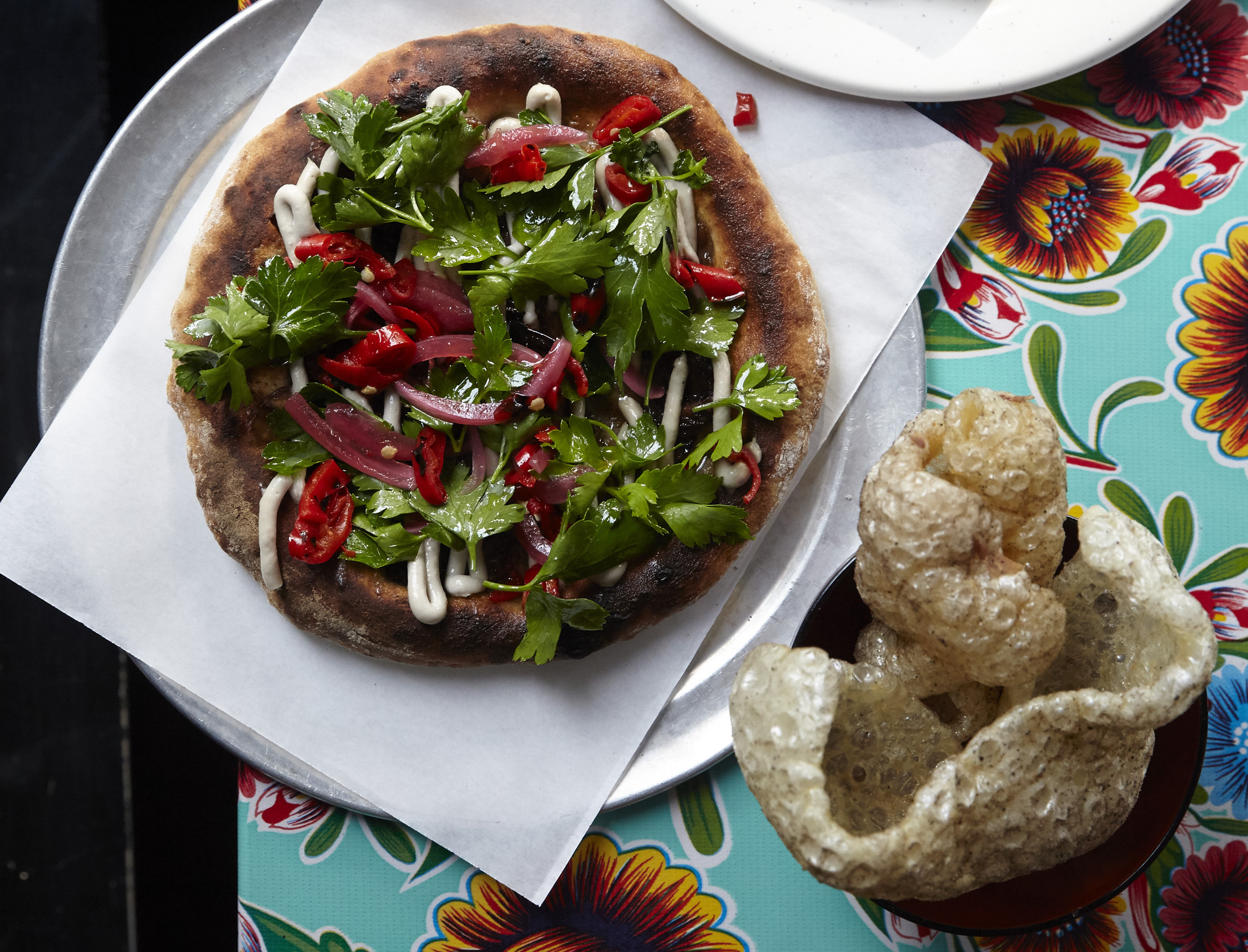 A lamb offal flatbread and pork crackling at Black Axe Mangal, featuring flowery tablecloths