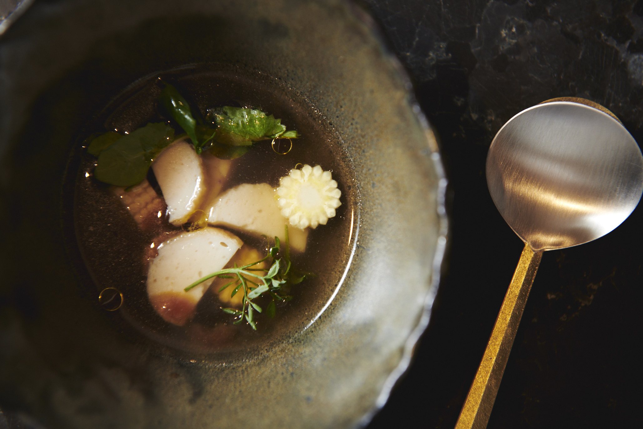 Guk soup with burdock, fish cakes, baby corn, and plum blossom fill a third of a dark, earthenware bowl