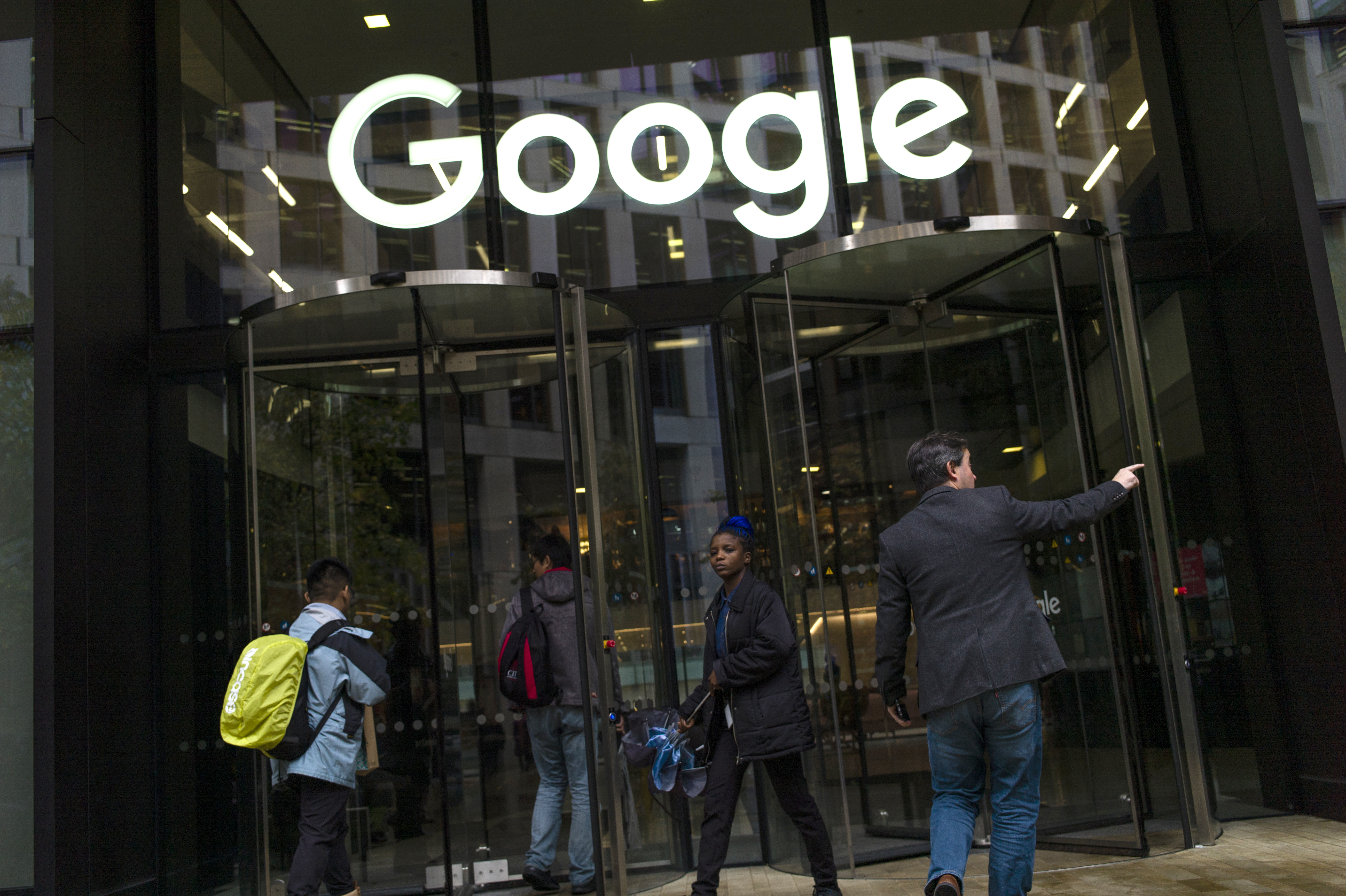 Google employees walking through a glass door under a sign reading “Google.”