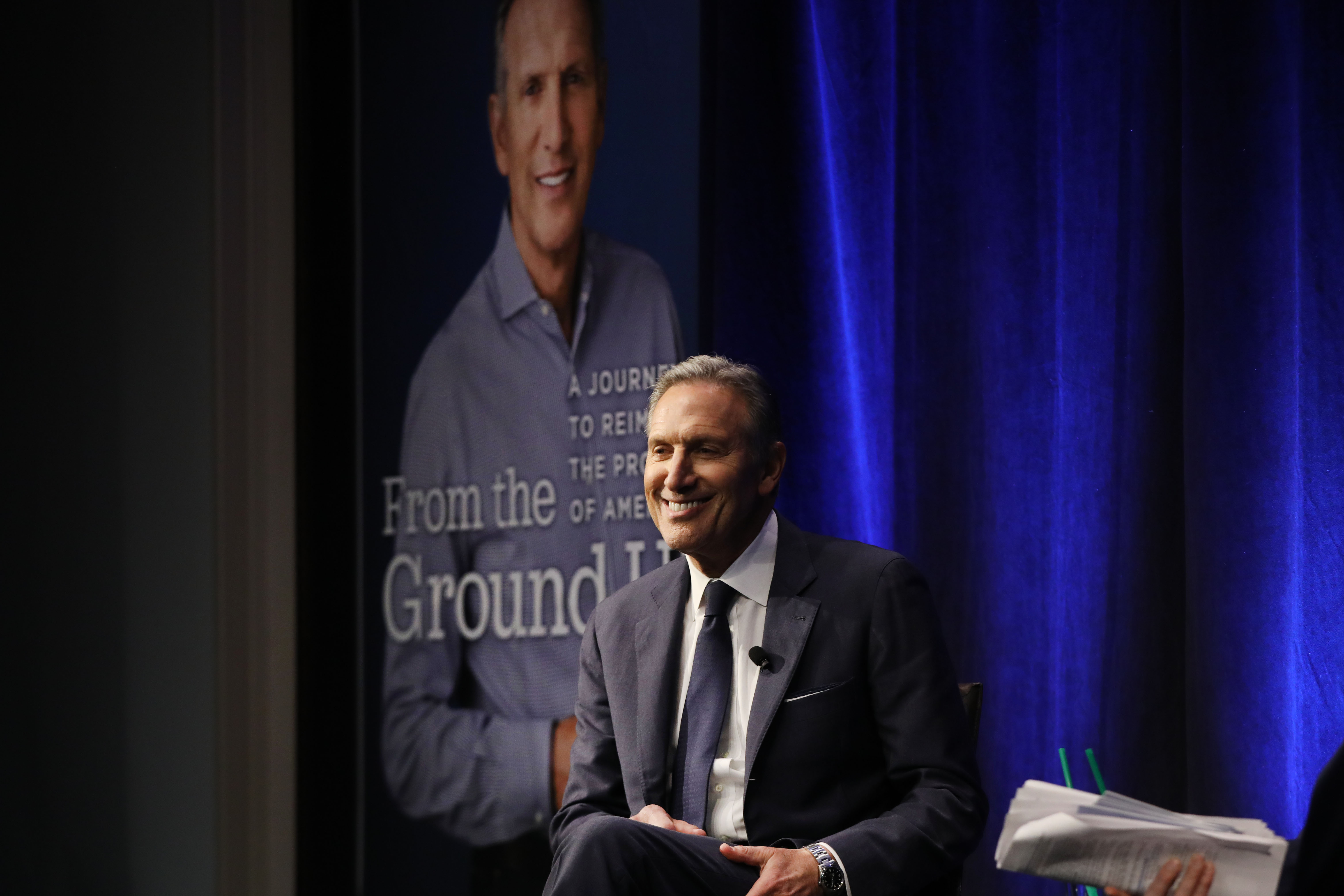 Former Starbucks CEO Howard Schultz onstage in front of a picture of his book.