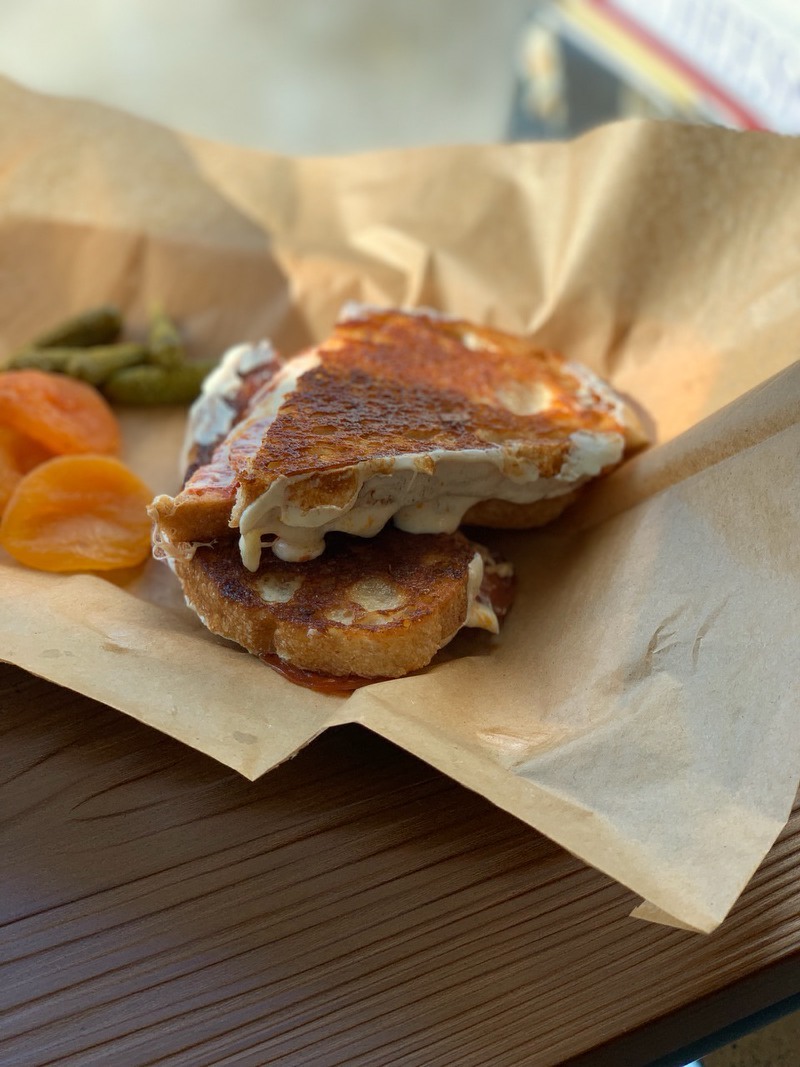 A grilled cheese sandwich sliced in half on brown paper next to apricots and pickles. 
