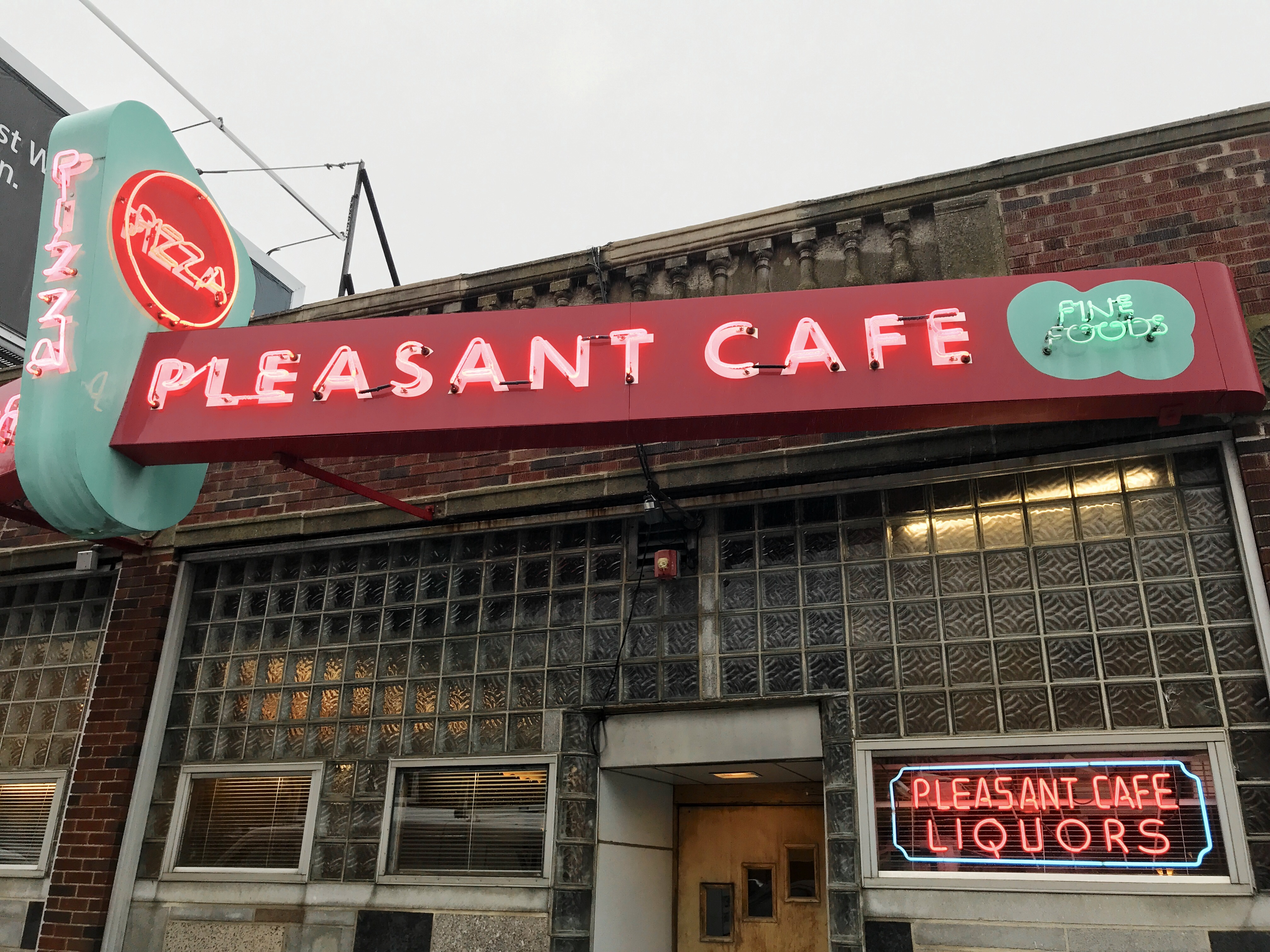 Exterior of an old-school restaurant with blue, pink, and red signage, including neon accents, that reads Pleasant Cafe.