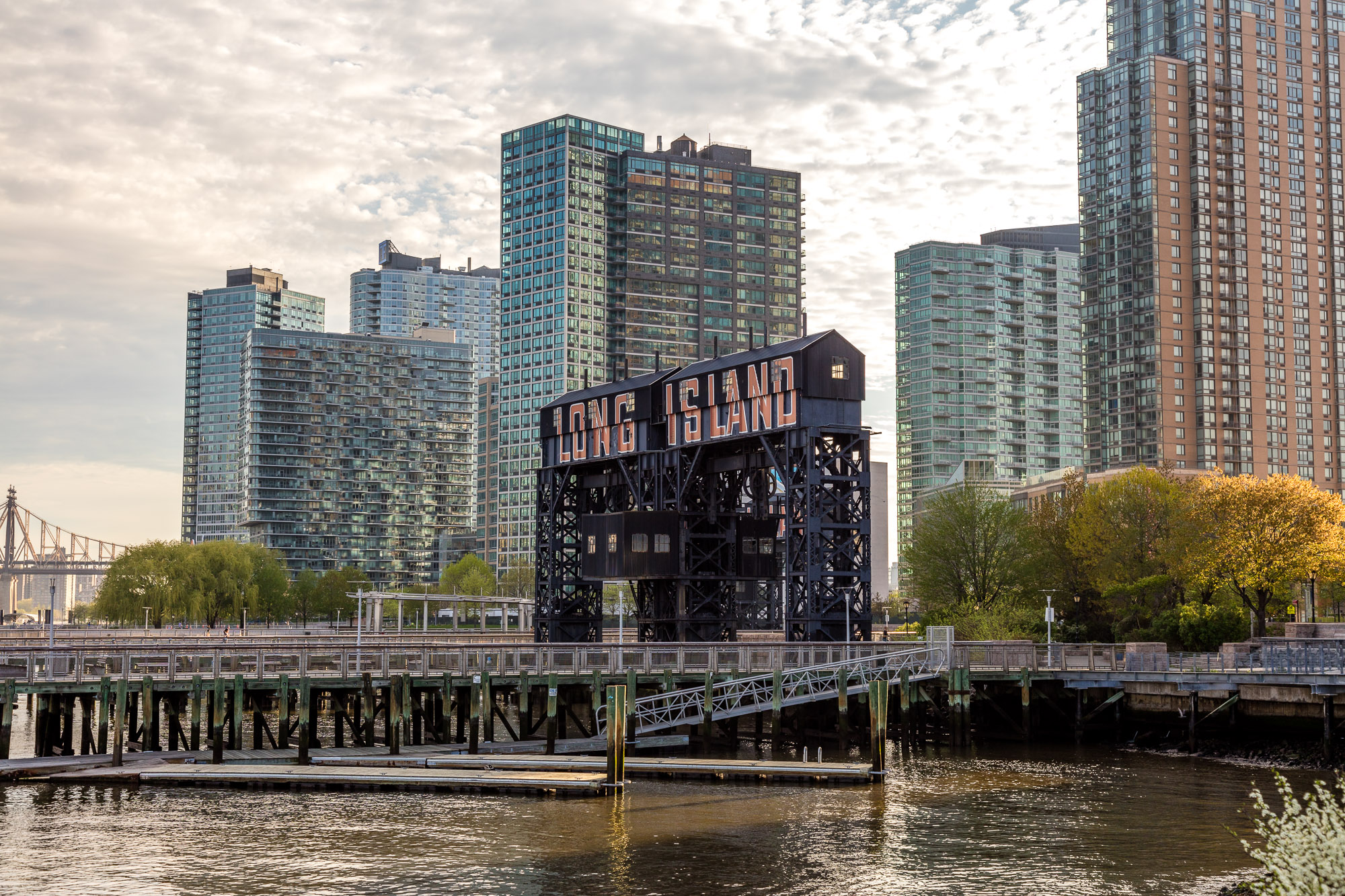 The waterfront in Long Island City. There is a pier with a sign that reads: Long Island. Behind the sign are many tall apartment buildings.